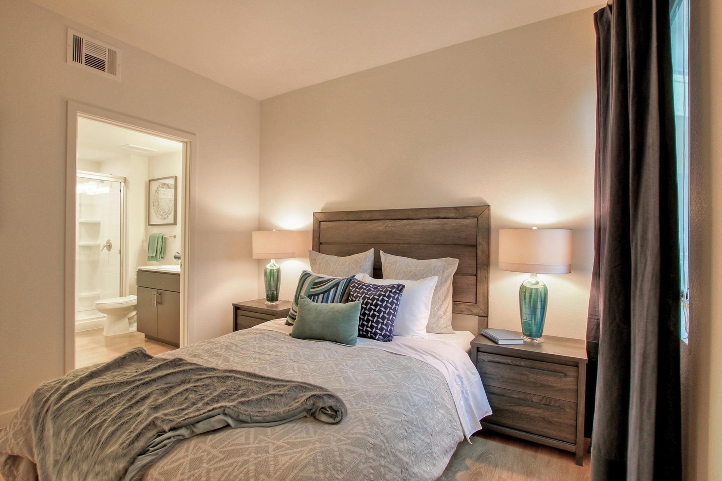 A cozy bedroom featuring a neatly made bed with decorative pillows, two bedside lamps, and a textured throw blanket. 