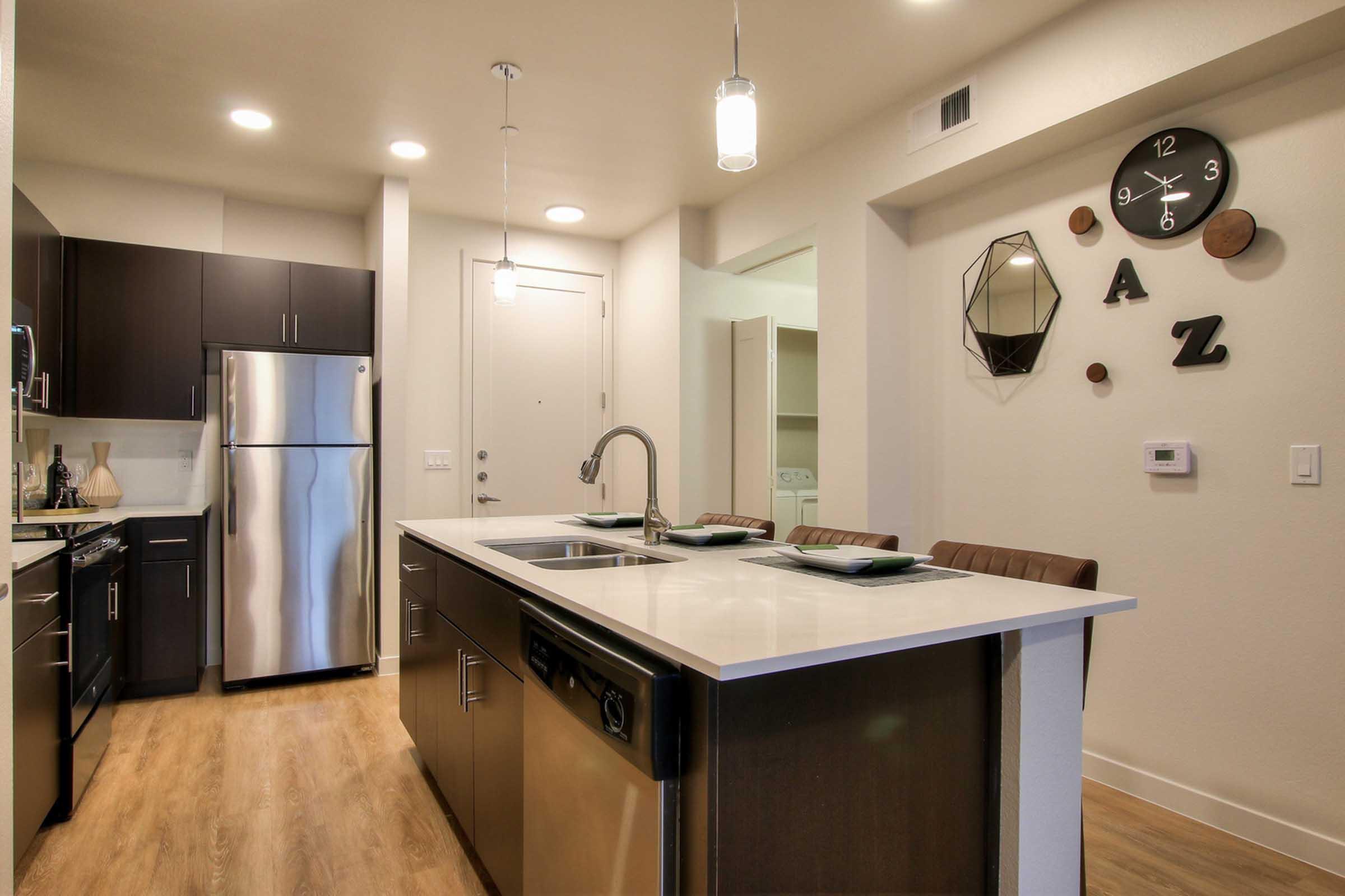 Modern kitchen featuring stainless steel appliances, a central island with a sink, sleek cabinetry, and stylish light fixtures. 