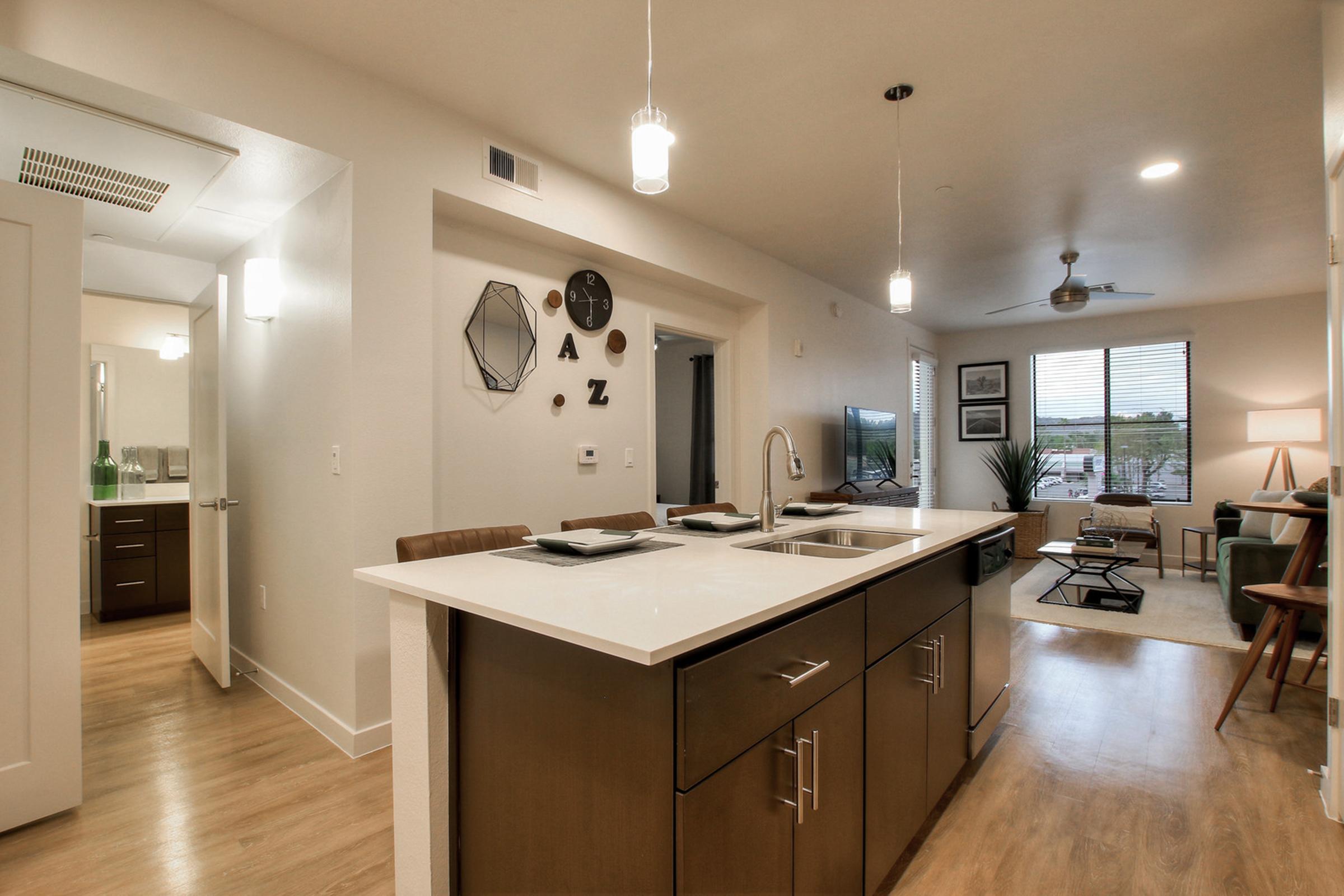 Modern kitchen and living area with an open layout. Features a central island with a sink, stylish cabinetry, and decorative wall art. 