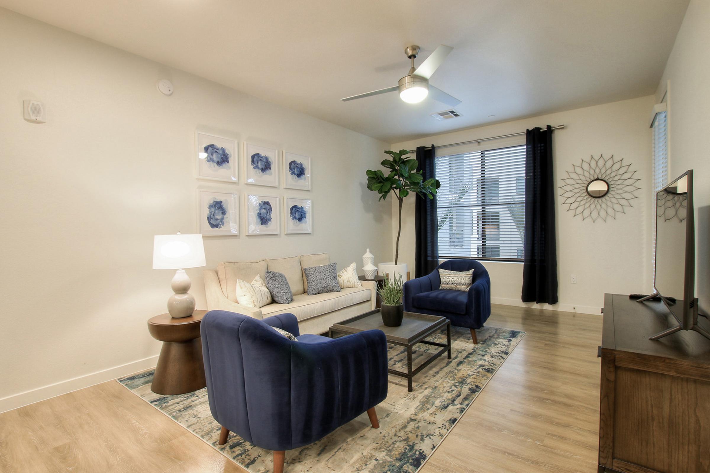 A modern living room featuring a light-colored sofa with decorative pillows, two blue armchairs, a dark wooden coffee table, and a floor lamp. 