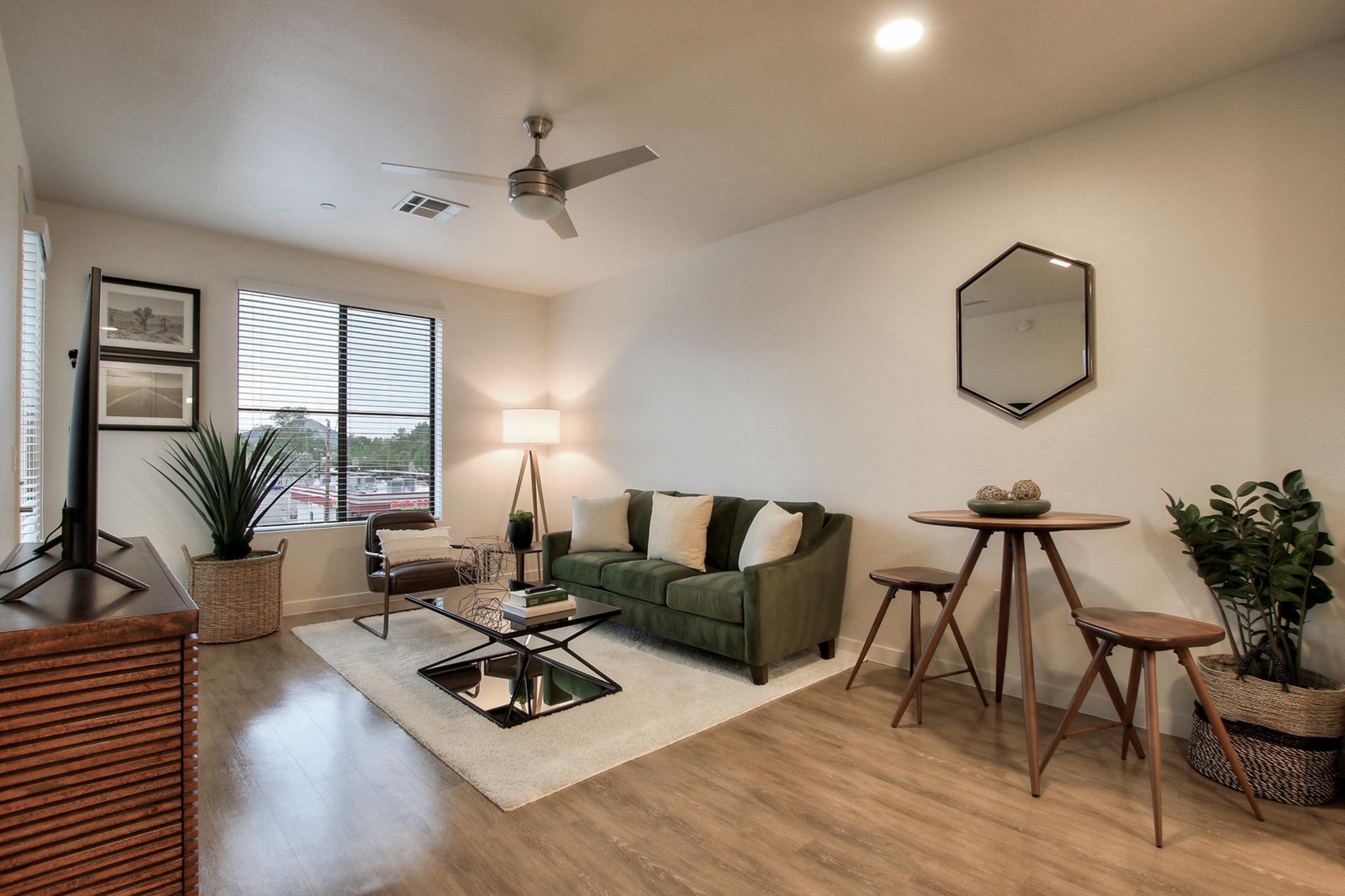 A modern living room featuring a green sofa with white and brown accent pillows, a glass coffee table on a light rug, and a tall floor lamp. 