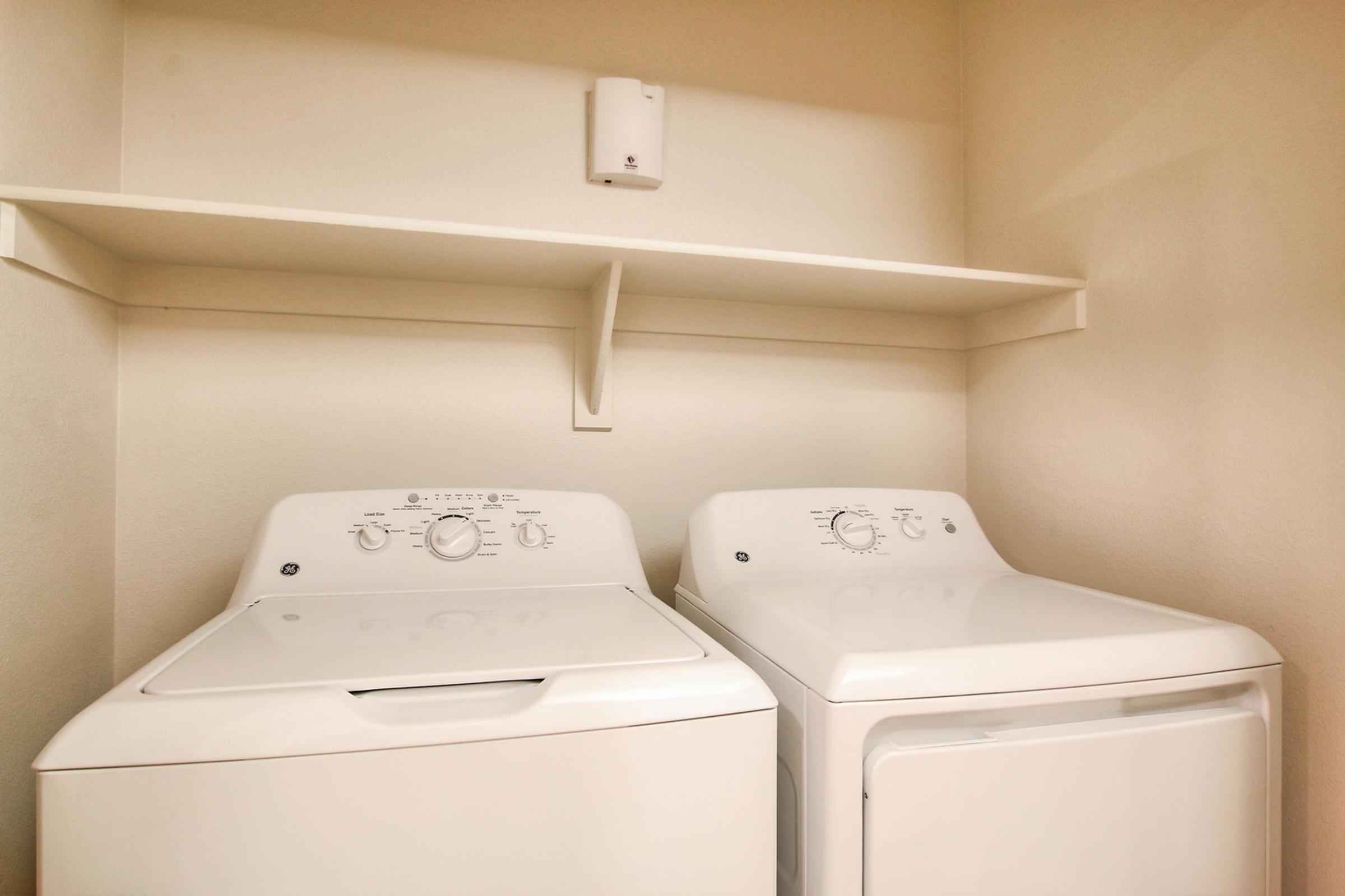 A clean laundry area featuring a white washing machine and dryer side by side, positioned against a plain wall.