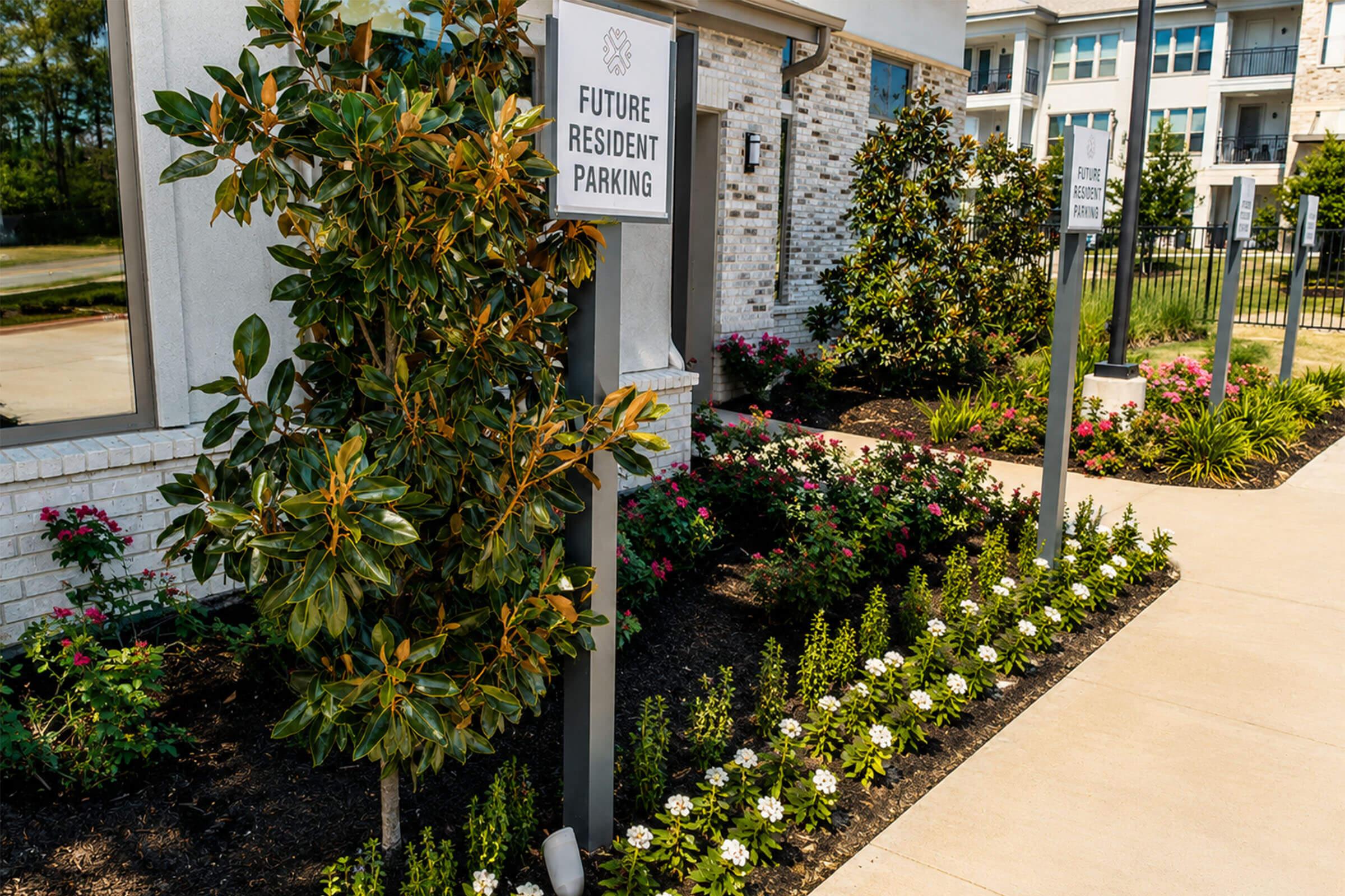 Signage indicating "Future Resident Parking" next to a landscaped area with flowers and greenery outside a modern residential building. The pathway is well maintained, and the surroundings include bushes and plants, suggesting a welcoming environment for future residents.