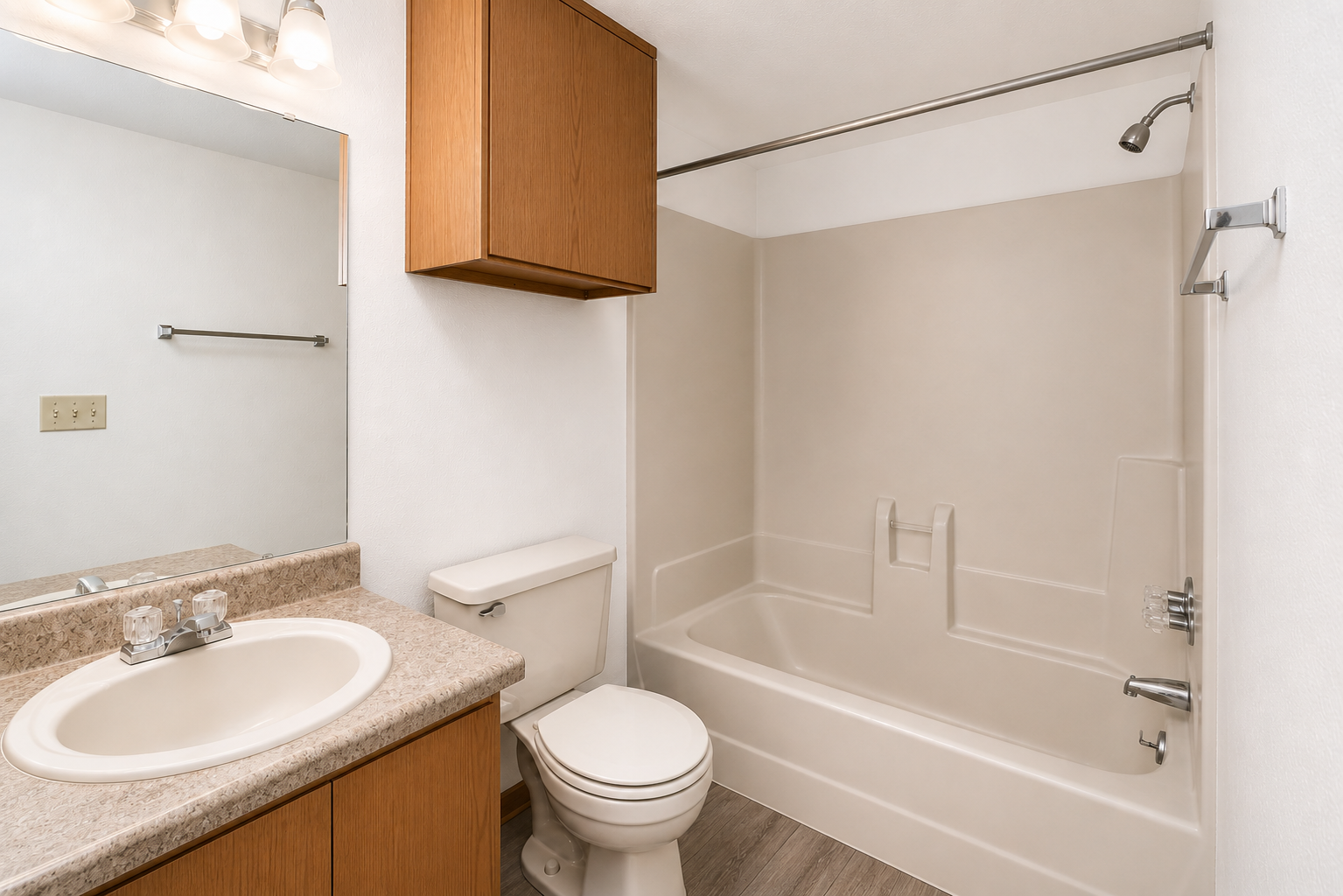 A clean and modern bathroom featuring a bathtub with a shower, a toilet, and a sink with a countertop. The walls are painted light, and there is a wooden cabinet above the sink. The floor has a wood-like finish, and there is a mirror above the sink reflecting the space.