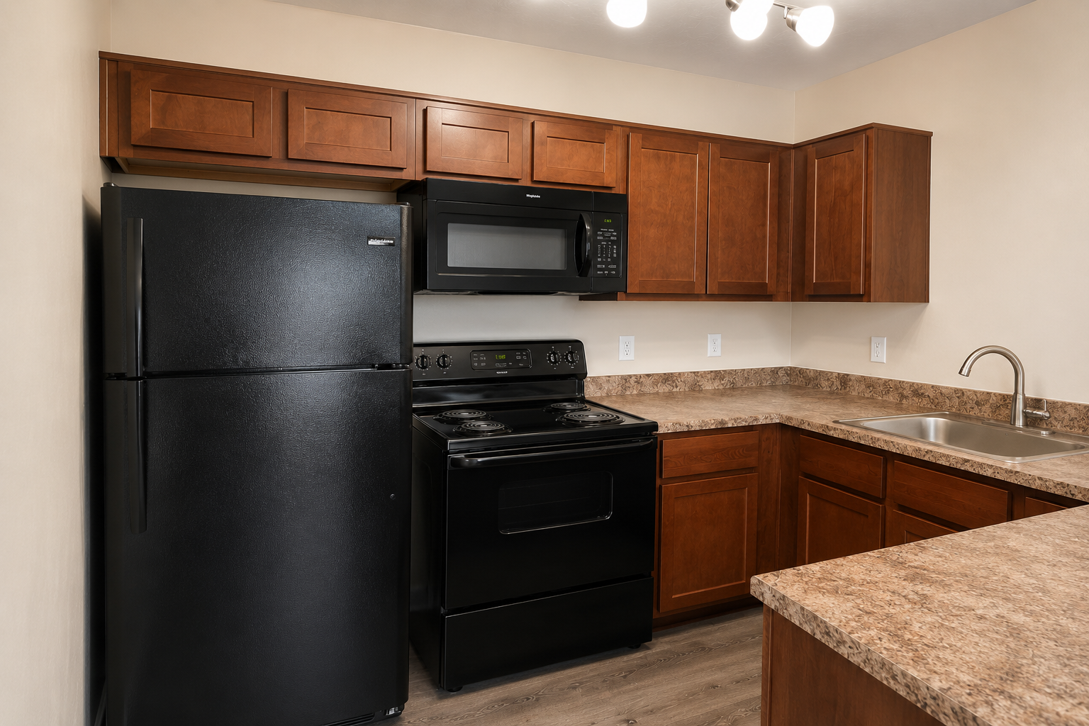 A modern kitchen featuring dark wood cabinets, a black refrigerator, black stove, and microwave. The countertops are light-colored, and a stainless steel sink is installed. The floor has a wood-like finish, and there are recessed lights in the ceiling. The overall design is contemporary and clean.