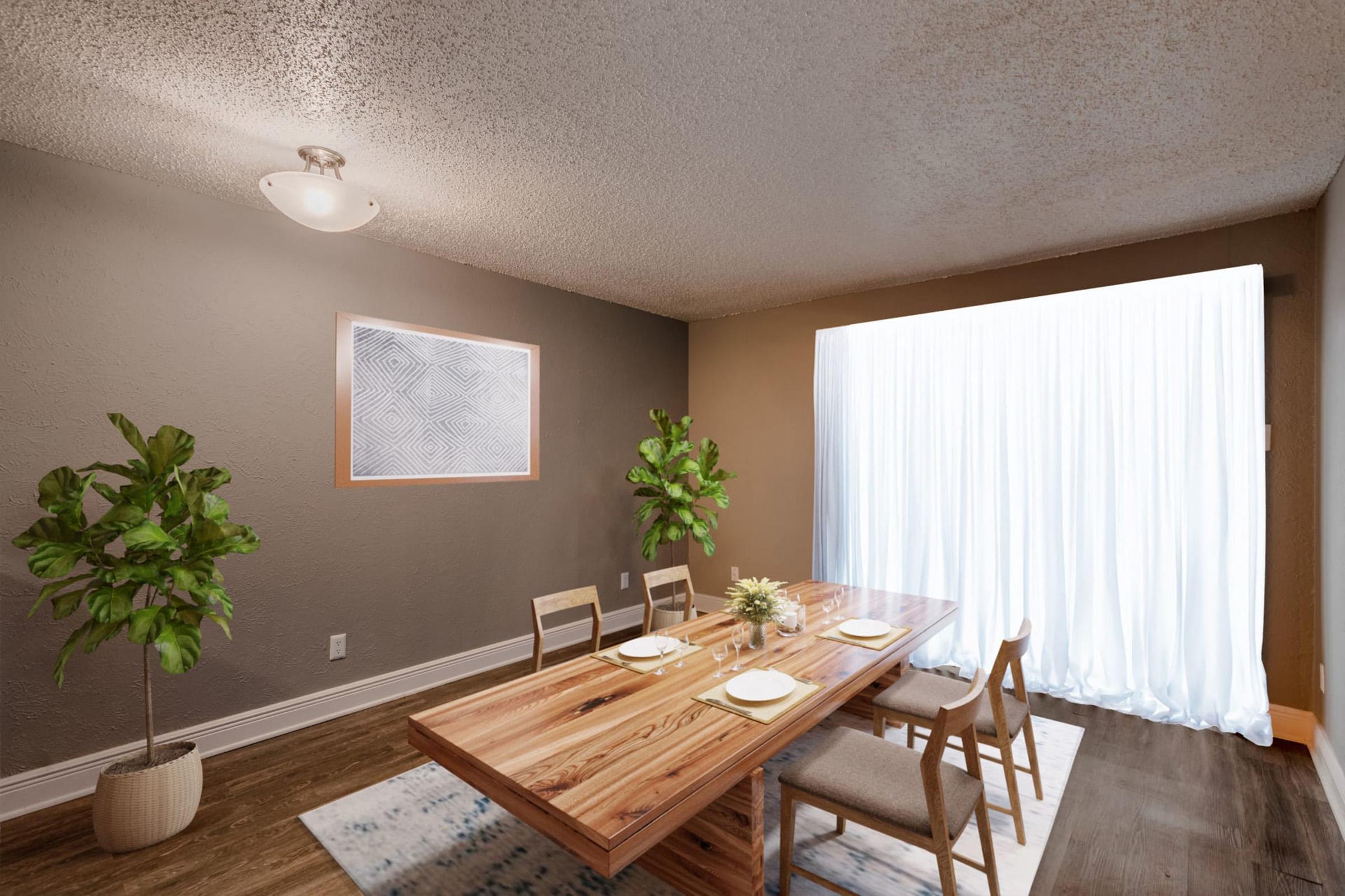 A modern dining room featuring a large wooden table set for four with plates and utensils. There are two potted plants in the corners, a piece of abstract wall art framed on one wall, and large curtains draping the window, allowing natural light to fill the space. The walls are painted in a neutral tone.