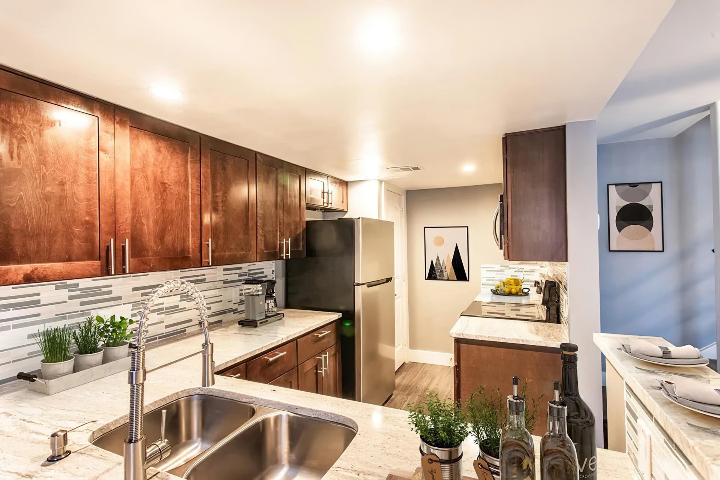 A modern kitchen featuring dark wood cabinets, a stylish backsplash, and a spacious countertop. It includes a stainless steel refrigerator, a sink with a contemporary faucet, and decorative plants. The overall design is sleek and inviting, with soft lighting enhancing the ambiance.