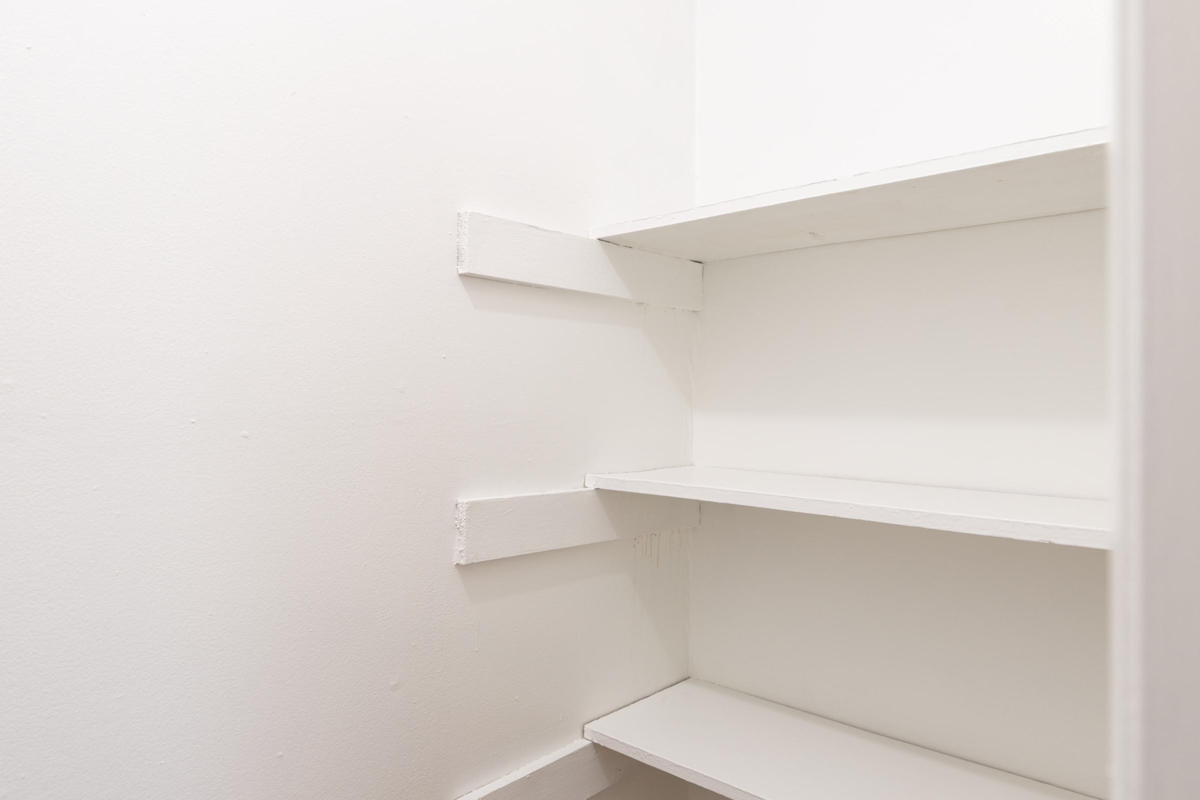 An empty, clean white closet with simple shelves. The walls and shelves are painted white, providing a minimalist and spacious appearance. There are no items on the shelves, creating a sense of organization and simplicity.