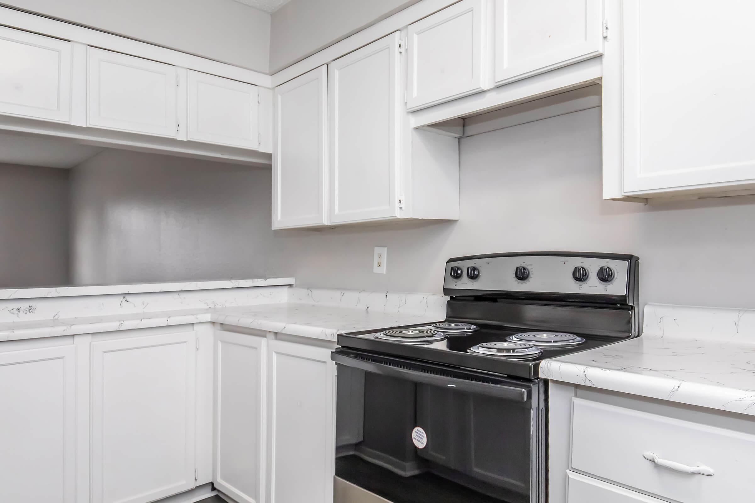 Modern kitchen featuring white cabinetry, a black electric stove, and a marble-like countertop. The design emphasizes a clean and airy aesthetic with a light color scheme, ideal for a contemporary living space.