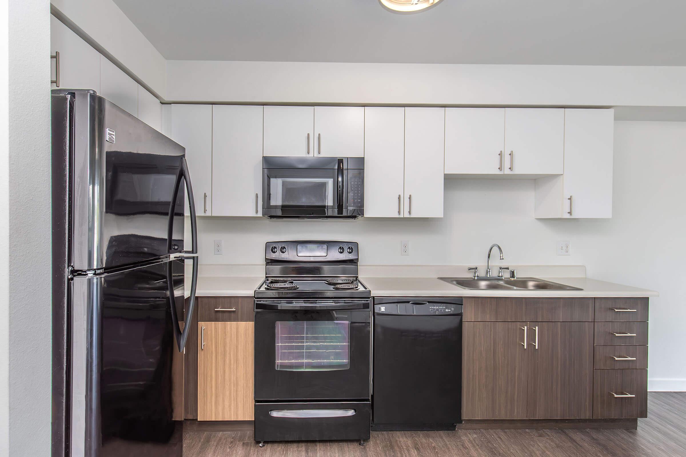 Modern kitchen with stainless steel appliances, including a black refrigerator, oven, microwave, and dishwasher. The cabinetry features a mix of white and dark wood finishes. A double sink is installed next to the stove. The kitchen has a clean and contemporary design with ample storage.