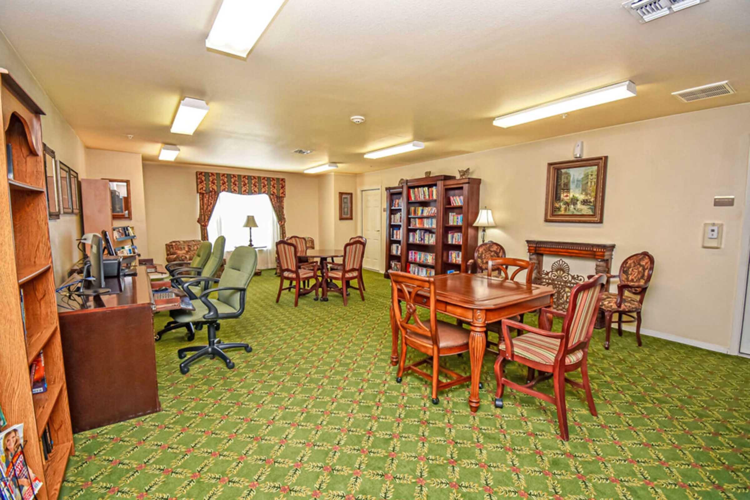 A well-lit common room featuring green carpeting and multiple seating areas.