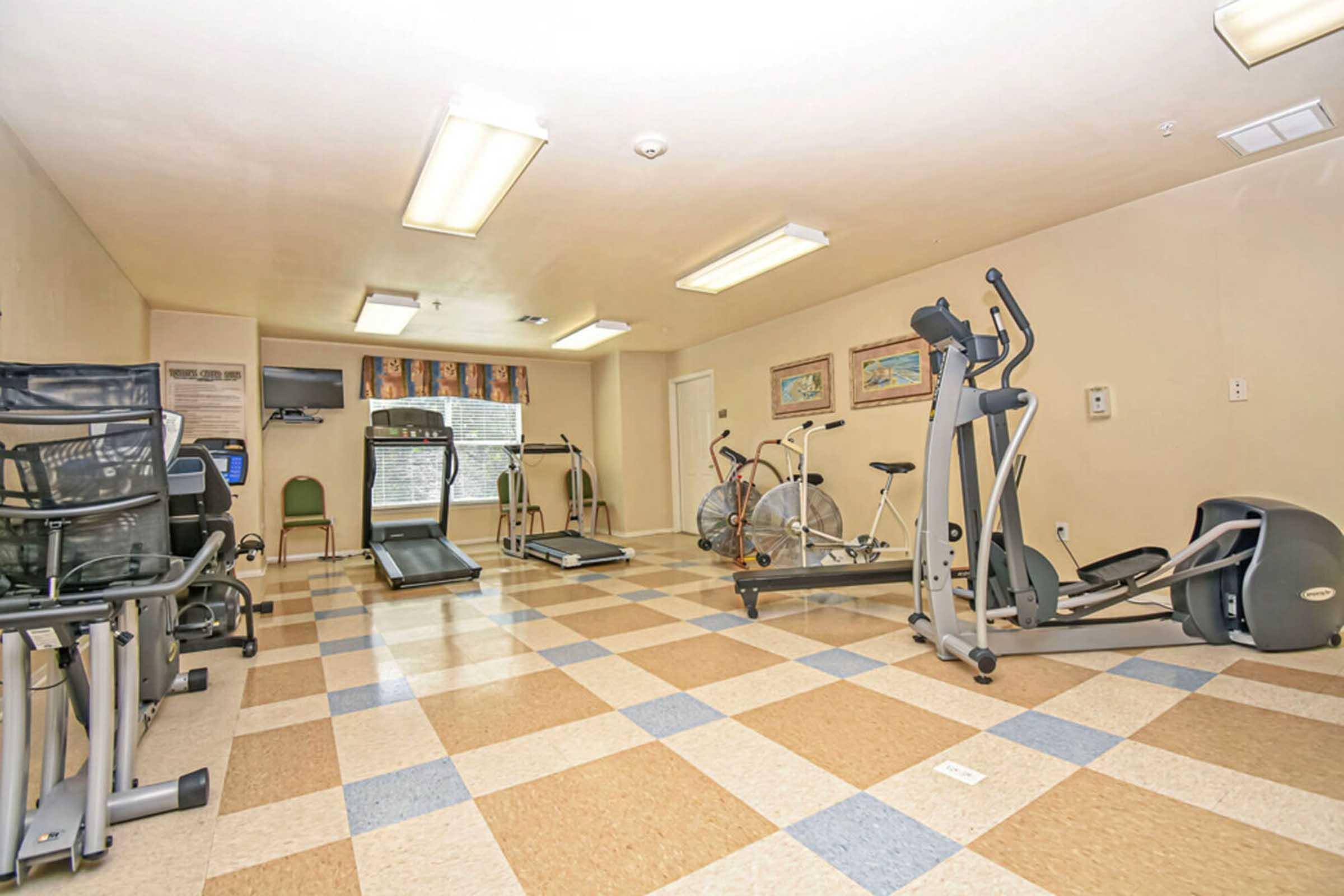 A well-lit fitness room featuring various exercise equipment, including treadmills, stationary bikes, elliptical machines, and a rowing machine.