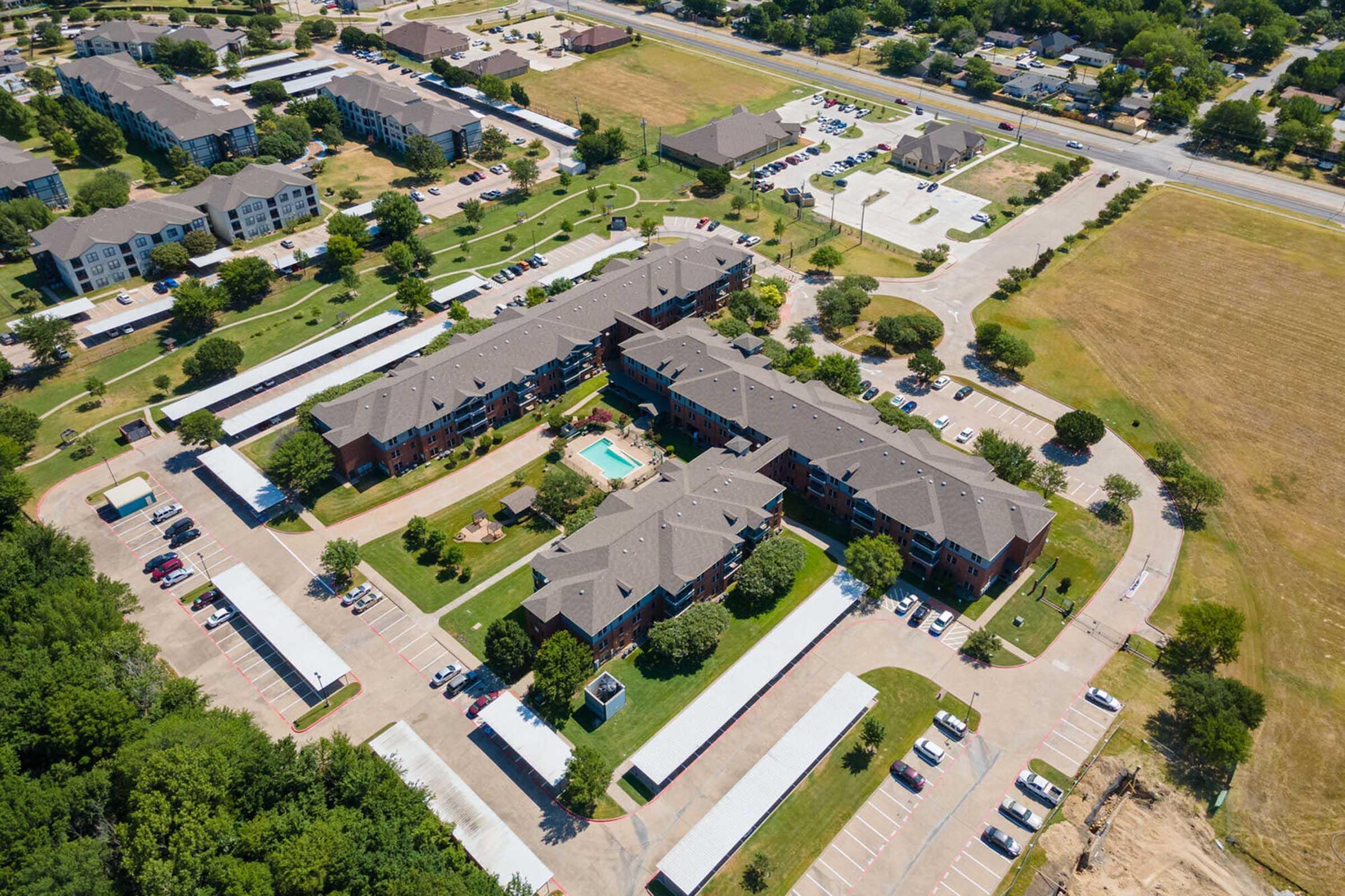 Aerial view of a residential complex featuring multiple buildings arranged around a central pool area.