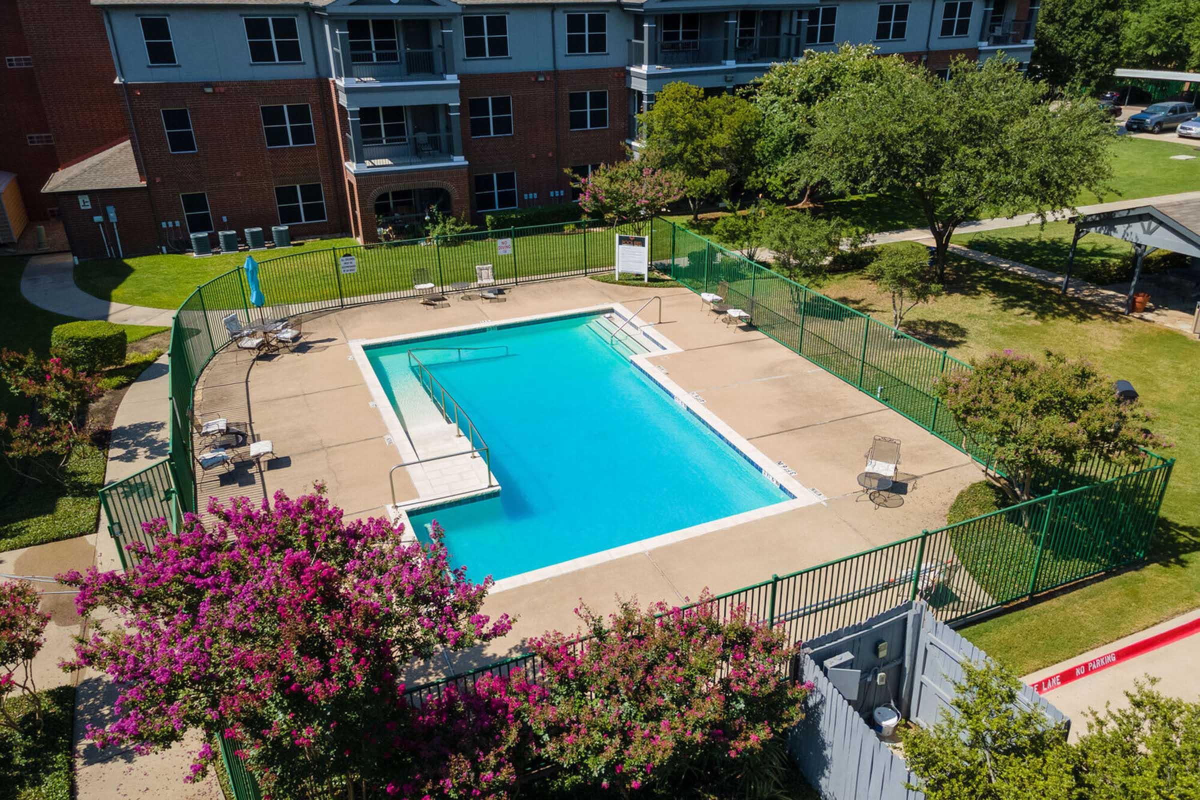Aerial view of a swimming pool surrounded by green fencing and lounge chairs.
