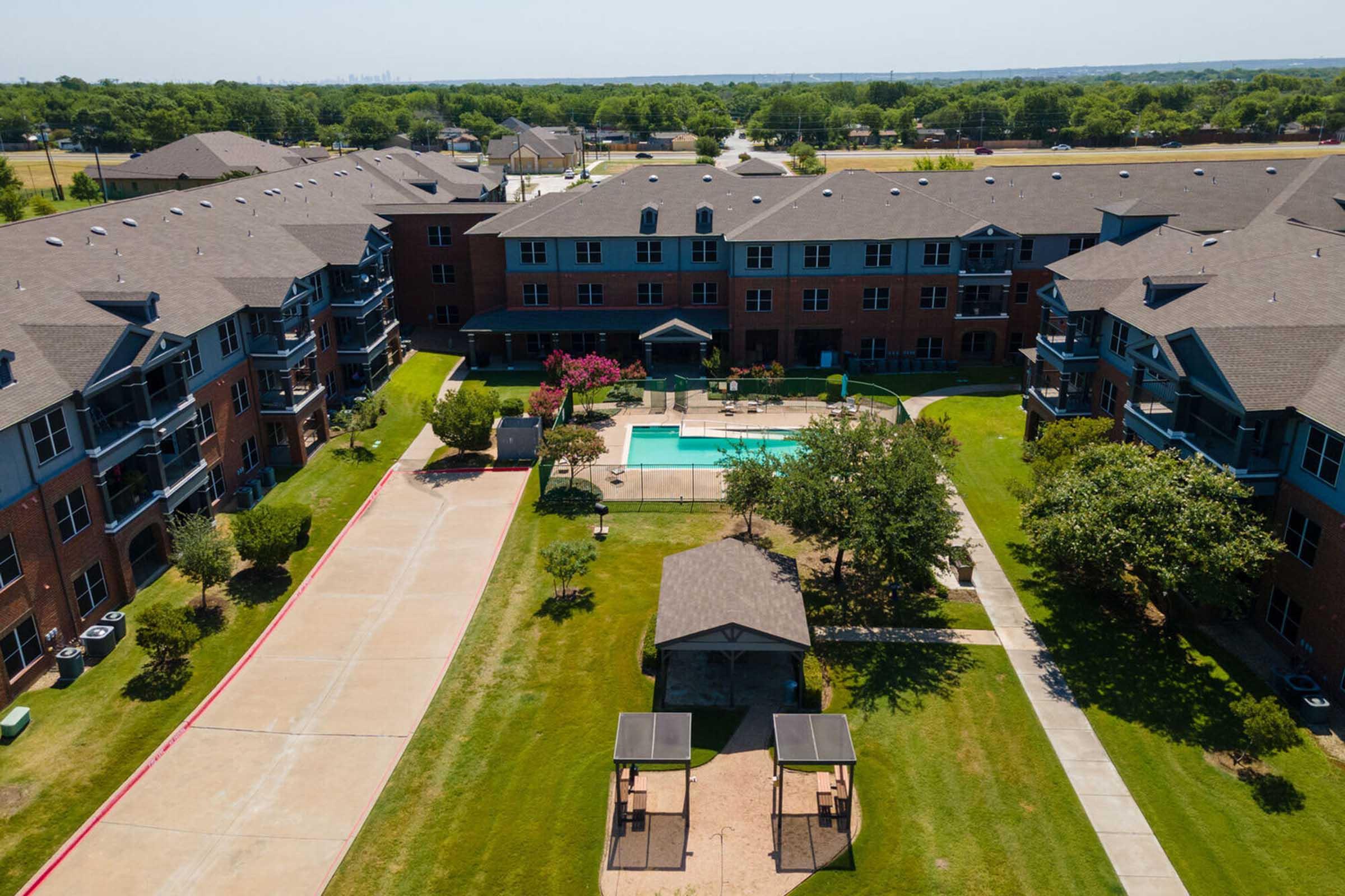 Aerial view of a multi-unit apartment complex featuring landscaped grounds, a swimming pool, and outdoor seating areas.