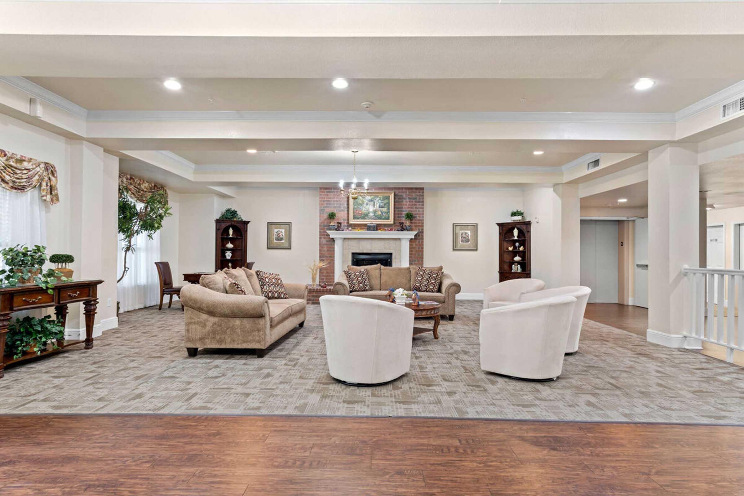 A spacious, well-lit living area featuring a cozy seating arrangement with two beige sofas and three white armchairs.
