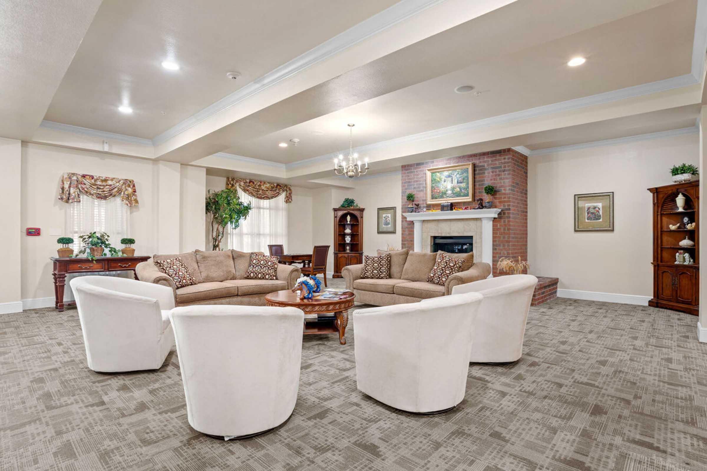 A spacious, well-lit living room featuring a set of beige sofas and white armchairs arranged around a wooden coffee table.
