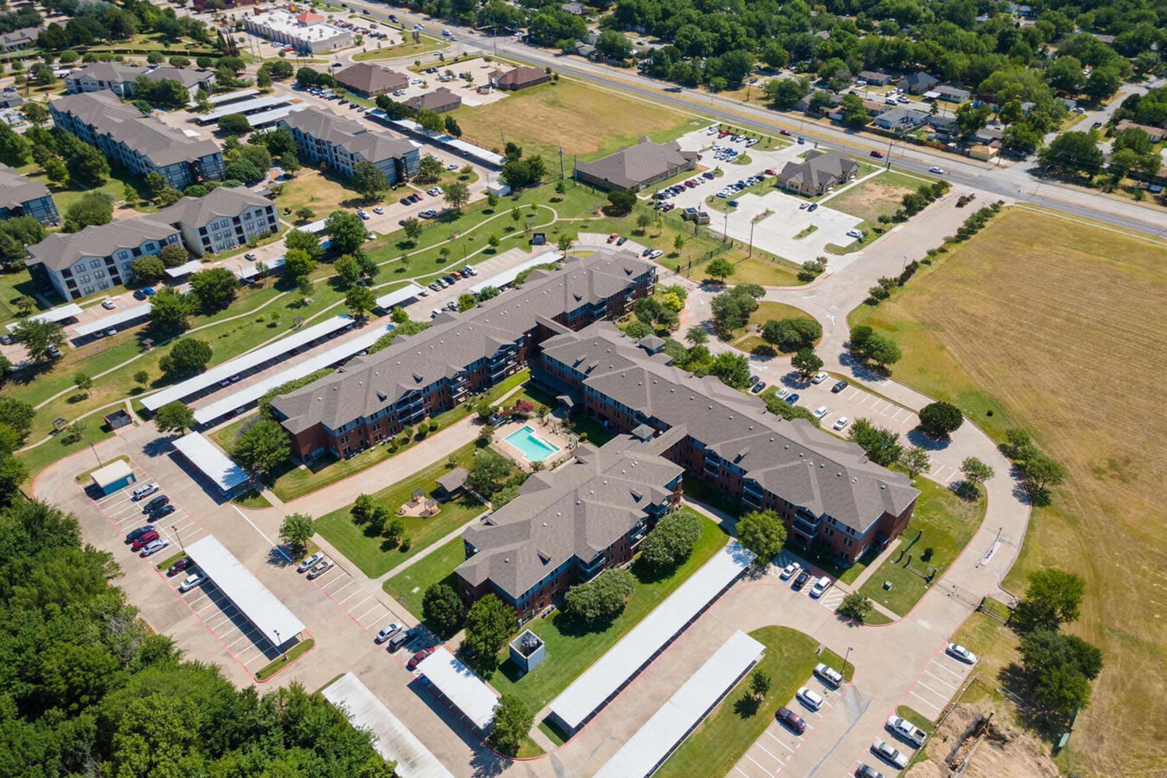 Aerial view of a residential area featuring several multi-story apartment buildings arranged around a central courtyard with a swimming pool.