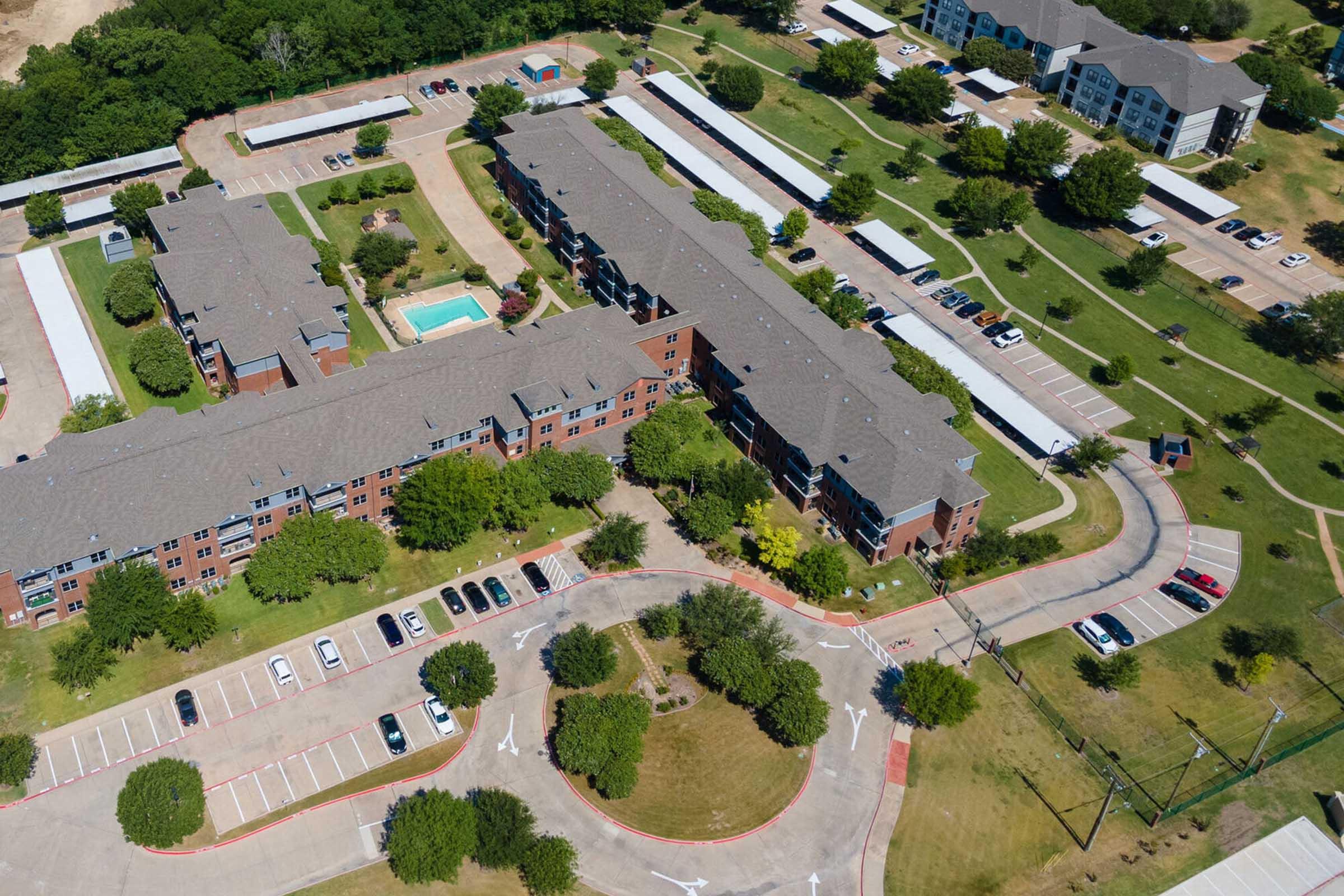 Aerial view of a residential area featuring multiple low-rise apartment buildings, a swimming pool, and parking lots.