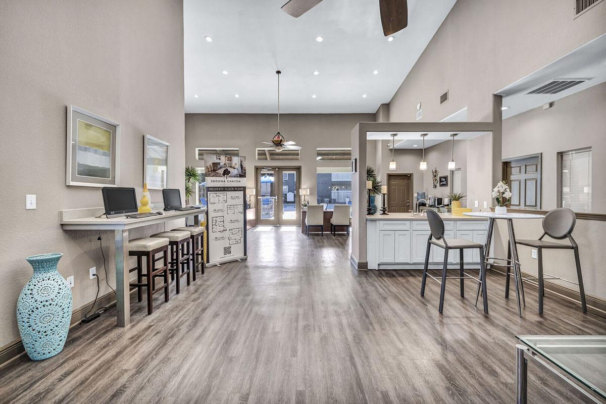 A modern interior of a spacious reception area featuring a light color palette, wooden flooring, two computer stations, and a seating area. Large windows allow natural light, and decorative elements include a turquoise vase and stylish furniture. The overall ambiance is welcoming and contemporary.