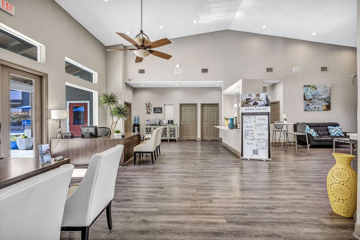 A spacious and modern lobby featuring a reception desk, stylish seating areas, and large windows. The decor includes plants, artwork, and a yellow vase. The high ceiling and neutral color palette create a welcoming atmosphere, with natural light enhancing the overall aesthetic.