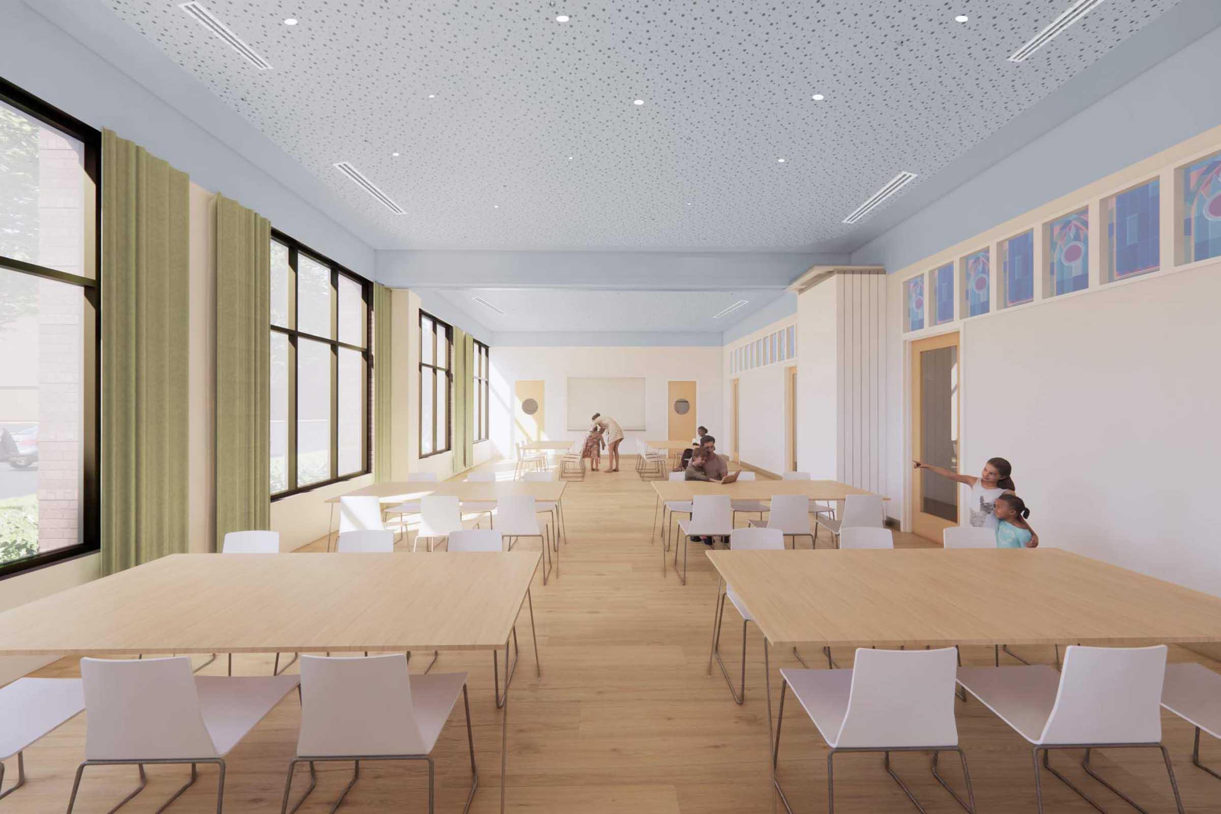 A spacious, well-lit interior of a modern hall featuring several wooden tables with white chairs. Large windows allow natural light to fill the space, and light blue walls complement the ceiling with decorative patterns. A few people are sitting and interacting, creating a welcoming atmosphere.