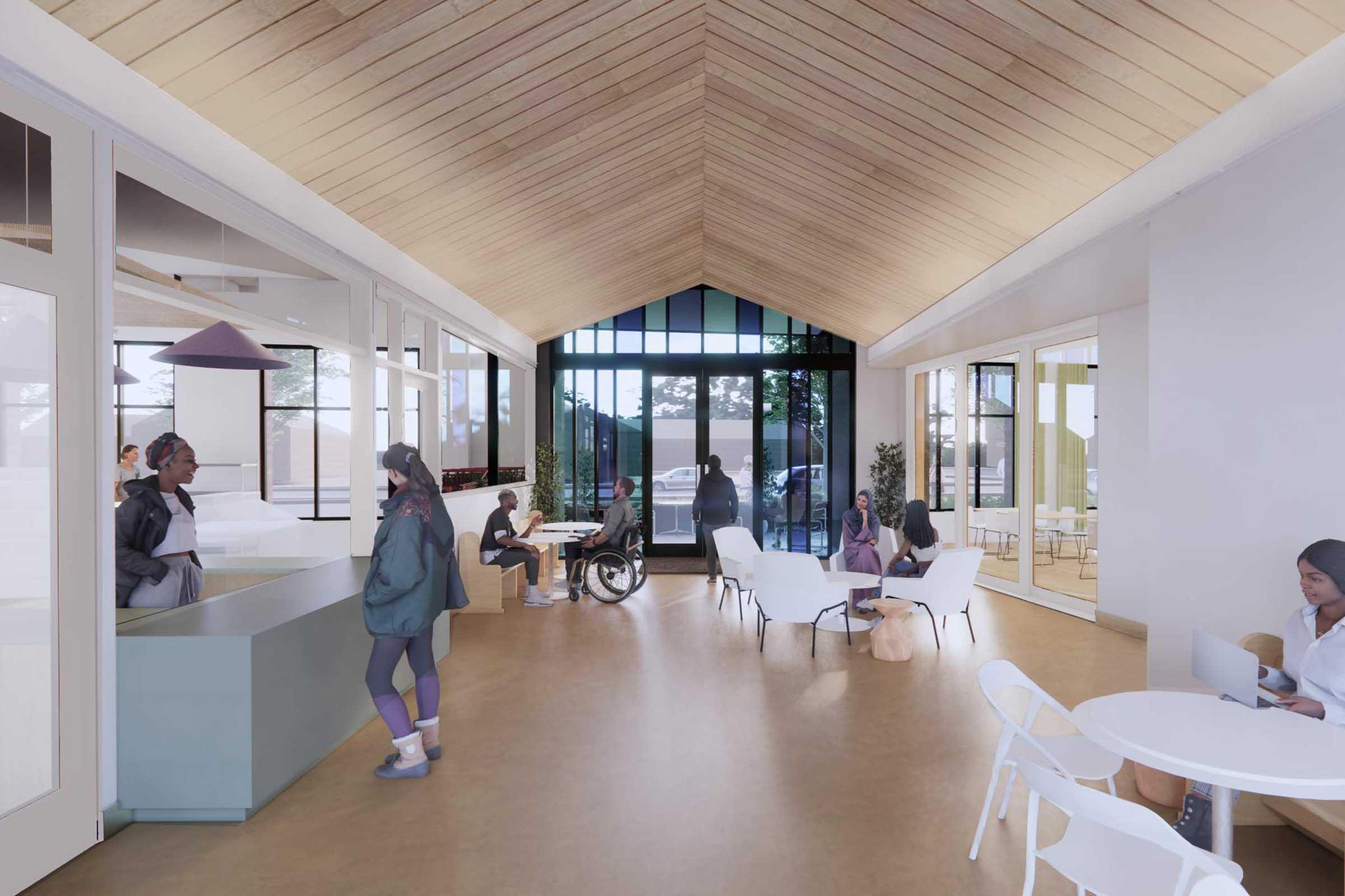 Interior view of a modern communal space featuring a high wooden ceiling, large windows letting in natural light, and a mix of seating options. People are engaged in various activities, including chatting, working, and using a wheelchair, creating an inviting and inclusive atmosphere.