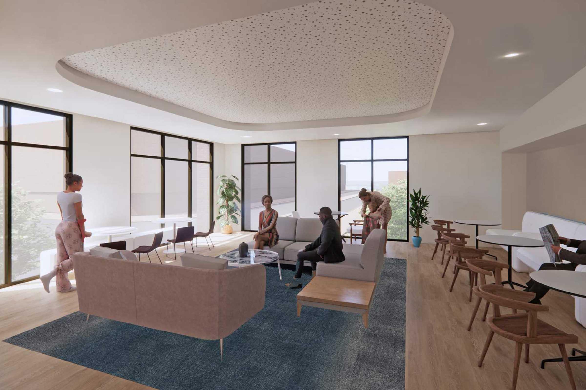 A modern lounge area with comfortable seating, featuring a light-colored sofa, chairs, and tables. A group of diverse individuals is engaged in conversation, while a woman stands nearby. Large windows provide natural light, and greenery adds a fresh touch to the interior design.