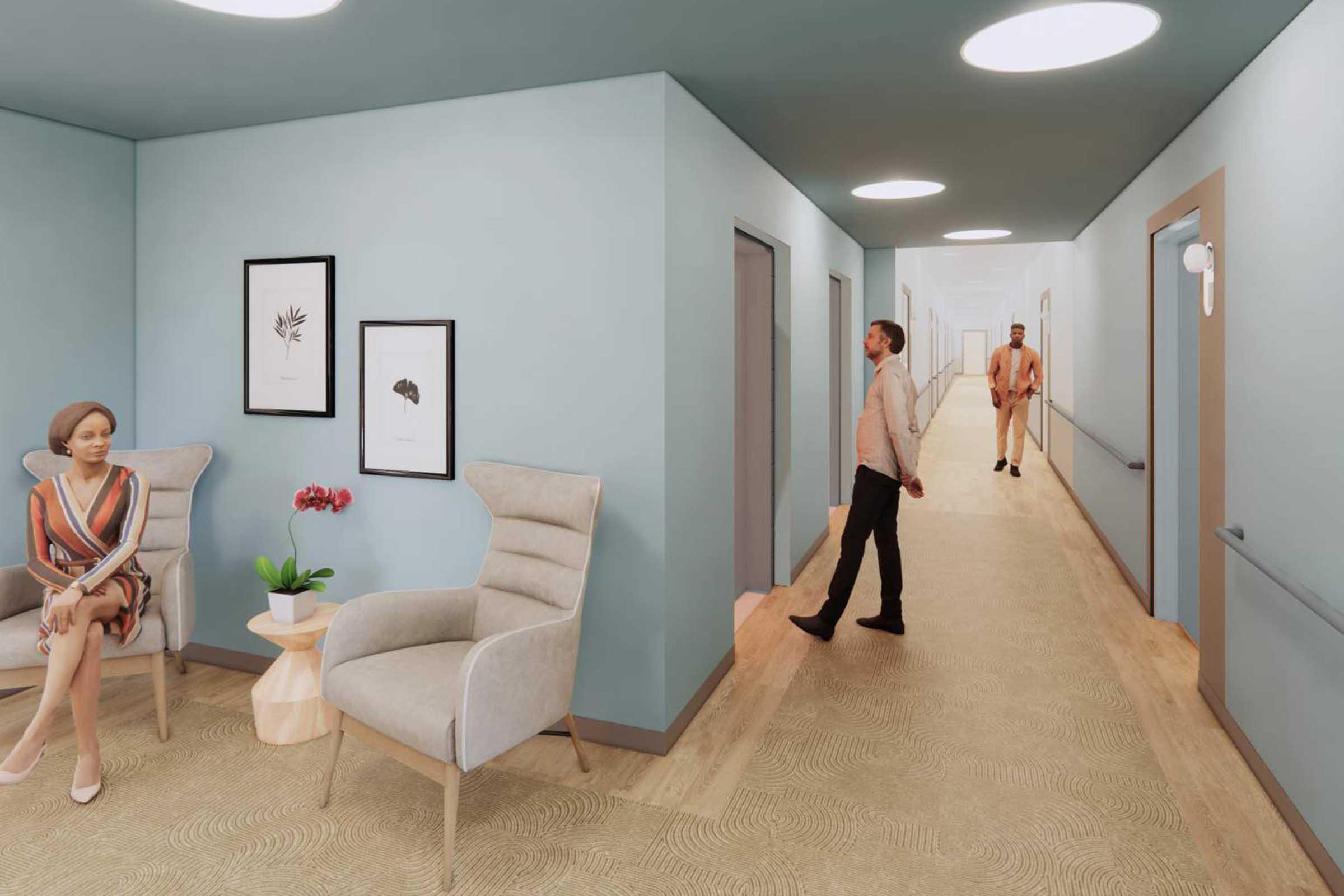 A modern, softly lit hallway in a healthcare setting. Two people are present: a woman sitting in a chair beside a small table with a plant, and a man walking in the corridor. The walls are painted light blue, with framed art on display. The flooring is light wood, creating a calming atmosphere.