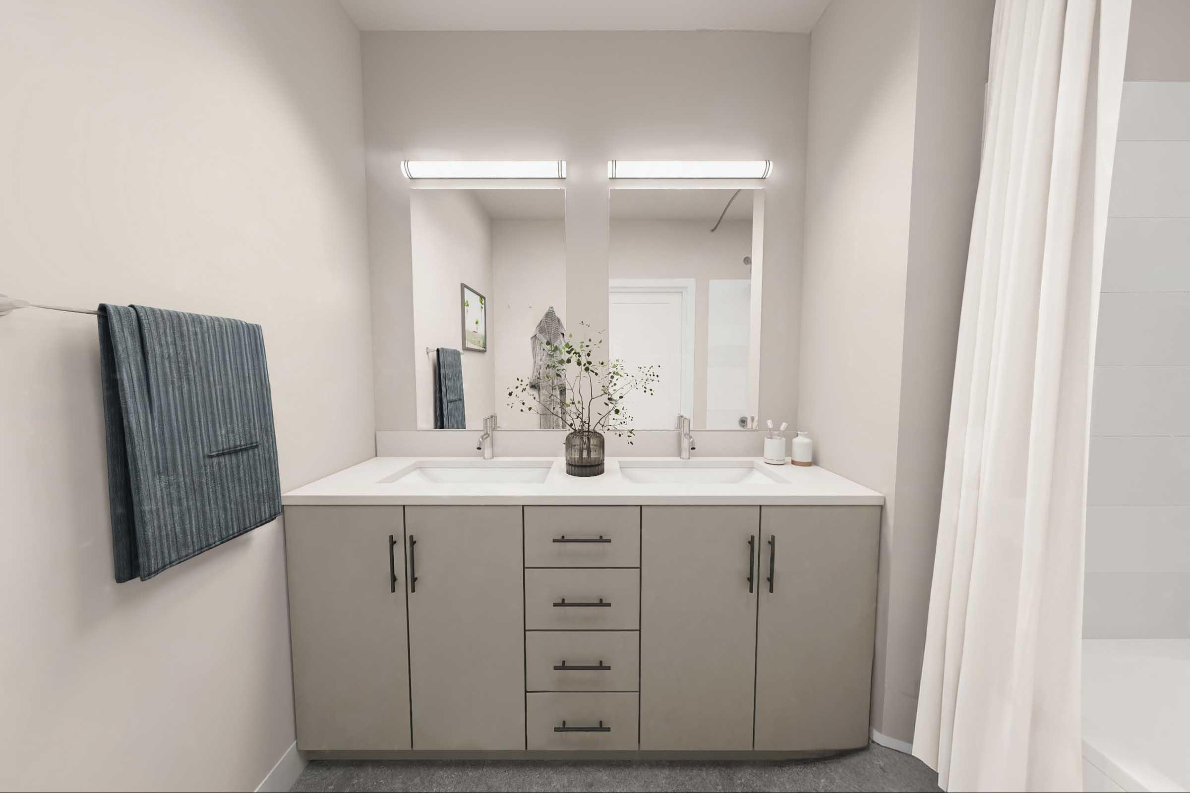 A modern bathroom featuring a dual sink vanity with a light gray cabinetry, two mirrors, and sleek silver fixtures. A potted plant decorates the countertop, while a blue towel hangs on the left. The room has neutral-colored walls and a shower area visible in the background.