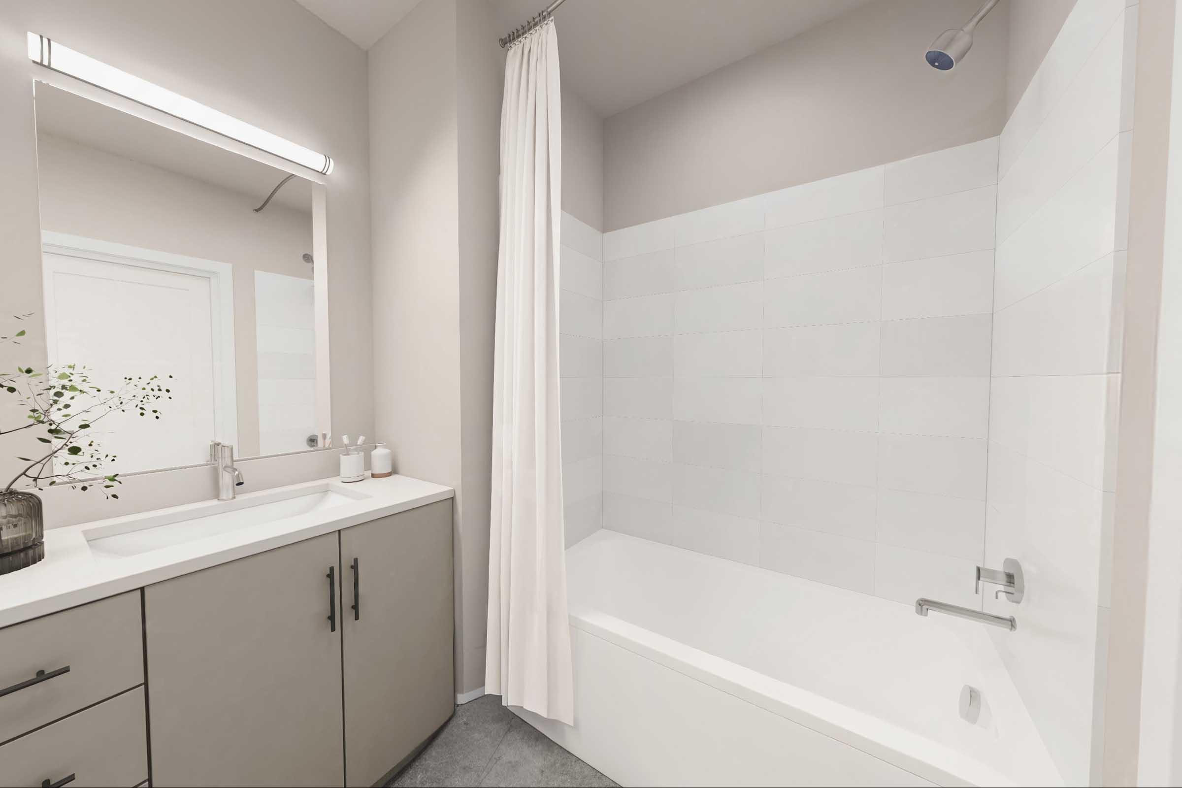 A modern bathroom featuring a bathtub with a shower, light-colored tiles, and a large mirror above a sink with contemporary cabinetry. The space is well-lit, with a neutral color scheme and a decorative vase with greenery on the countertop.