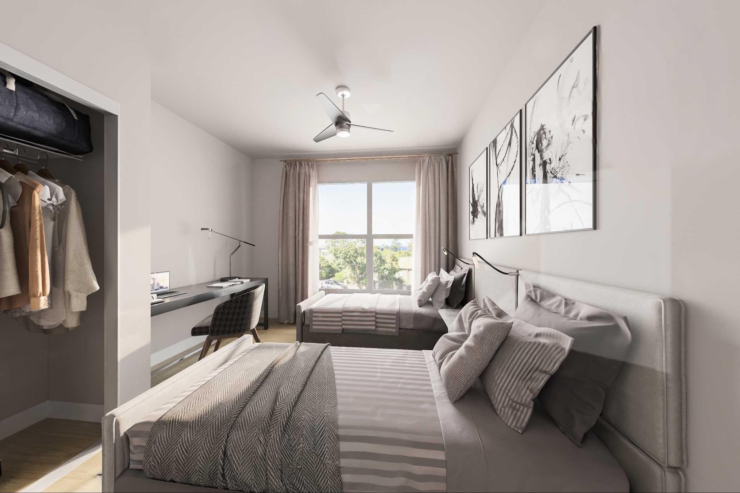 A modern bedroom featuring two twin beds with decorative pillows and bedding. There's a closet with clothes visible, a sleek desk with a chair, and a window allowing natural light to fill the space. The walls are adorned with framed artwork, and a ceiling fan is present.