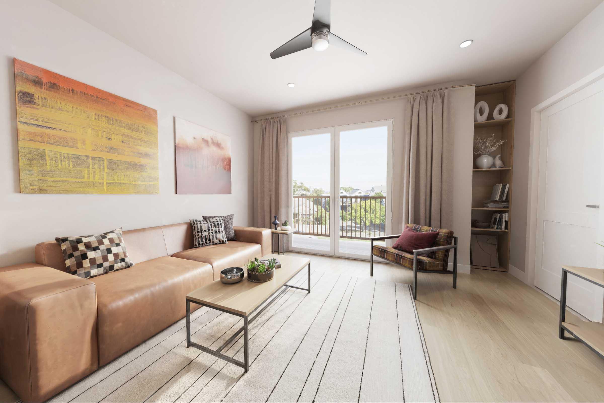 A modern living room featuring a brown leather sectional couch with decorative pillows, a wooden coffee table with plants, and a cozy armchair. Large glass doors open to a balcony, and the space is decorated with abstract artwork and a light rug on wooden flooring, illuminated by natural light.