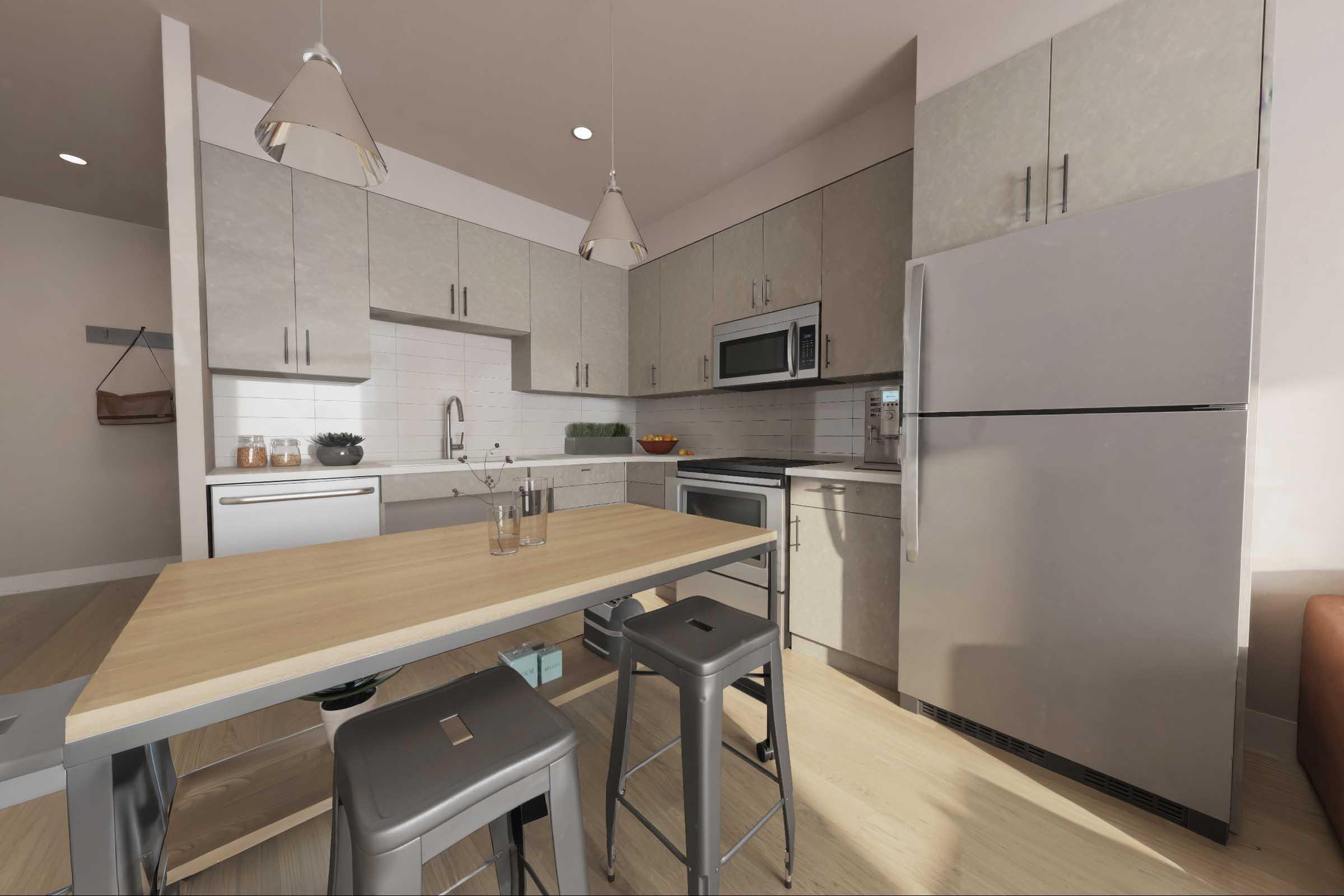 A modern kitchen featuring light gray cabinetry, stainless steel appliances, and a small wooden dining table with metal stools. The space is bright with natural light and has a minimalist design, including a sink, microwave, and refrigerator, with decorative items on the counter.