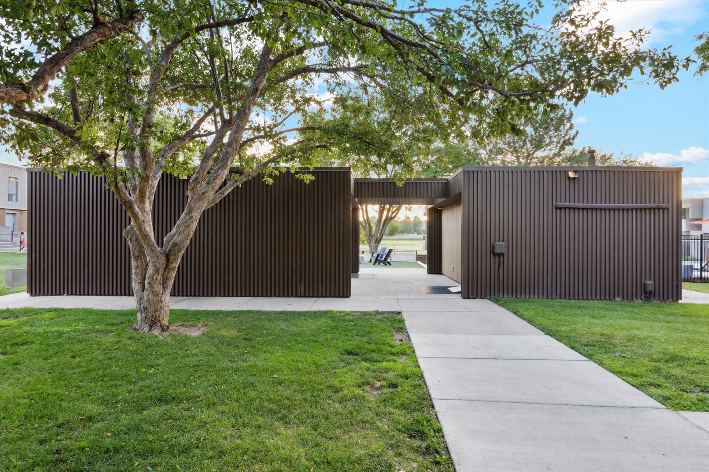 A modern building with a sleek, metallic facade nestled amidst green grass and trees. The structure features a minimalist design with sharp lines and a pathway leading to it, creating a contemporary architectural statement in a recreational area.