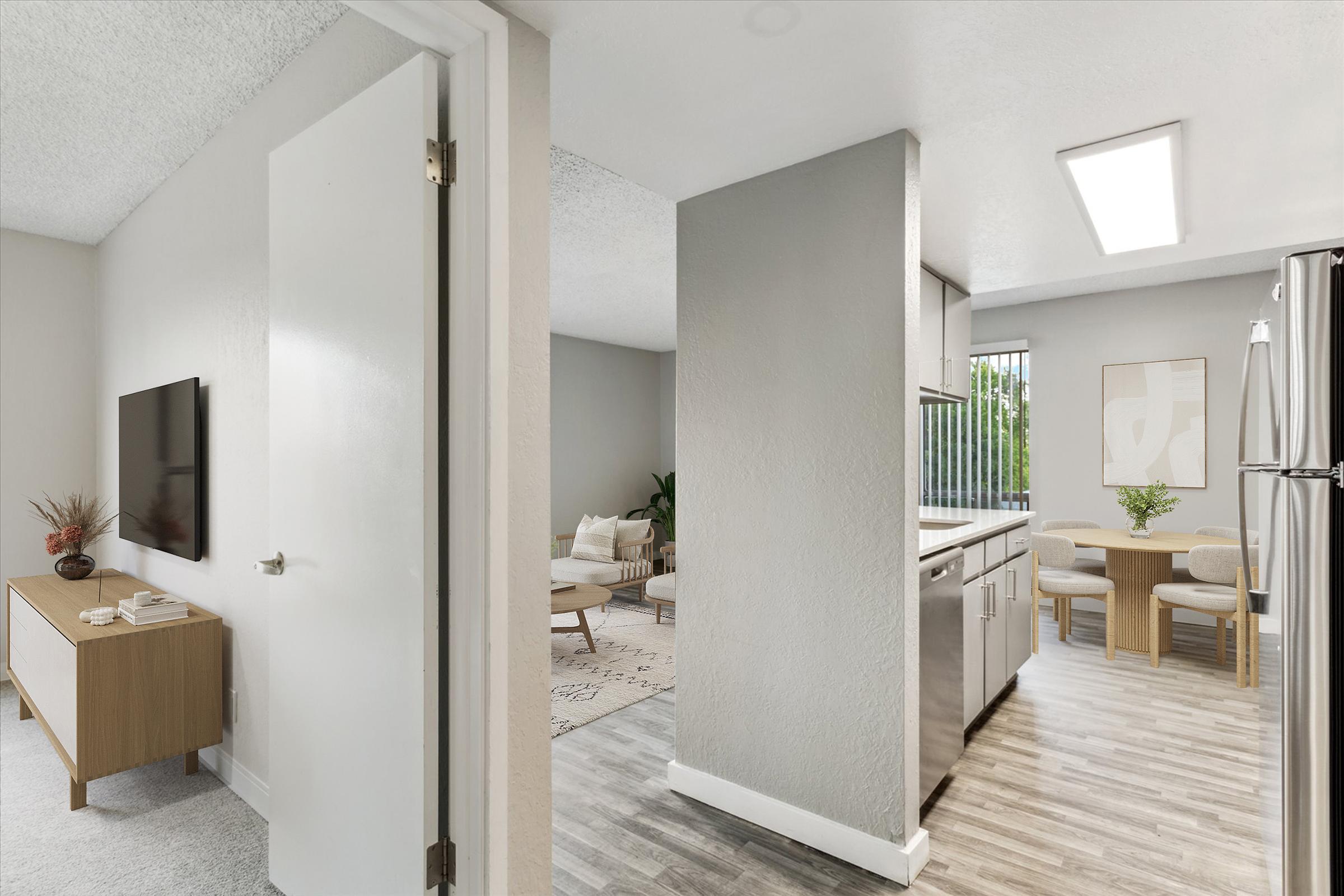 Interior view of a modern, well-lit open-concept living space featuring a kitchen with stainless steel appliances, a dining area with a small table and chairs, and a cozy seating area visible in the background. Light-colored walls and flooring create a bright, inviting atmosphere.
