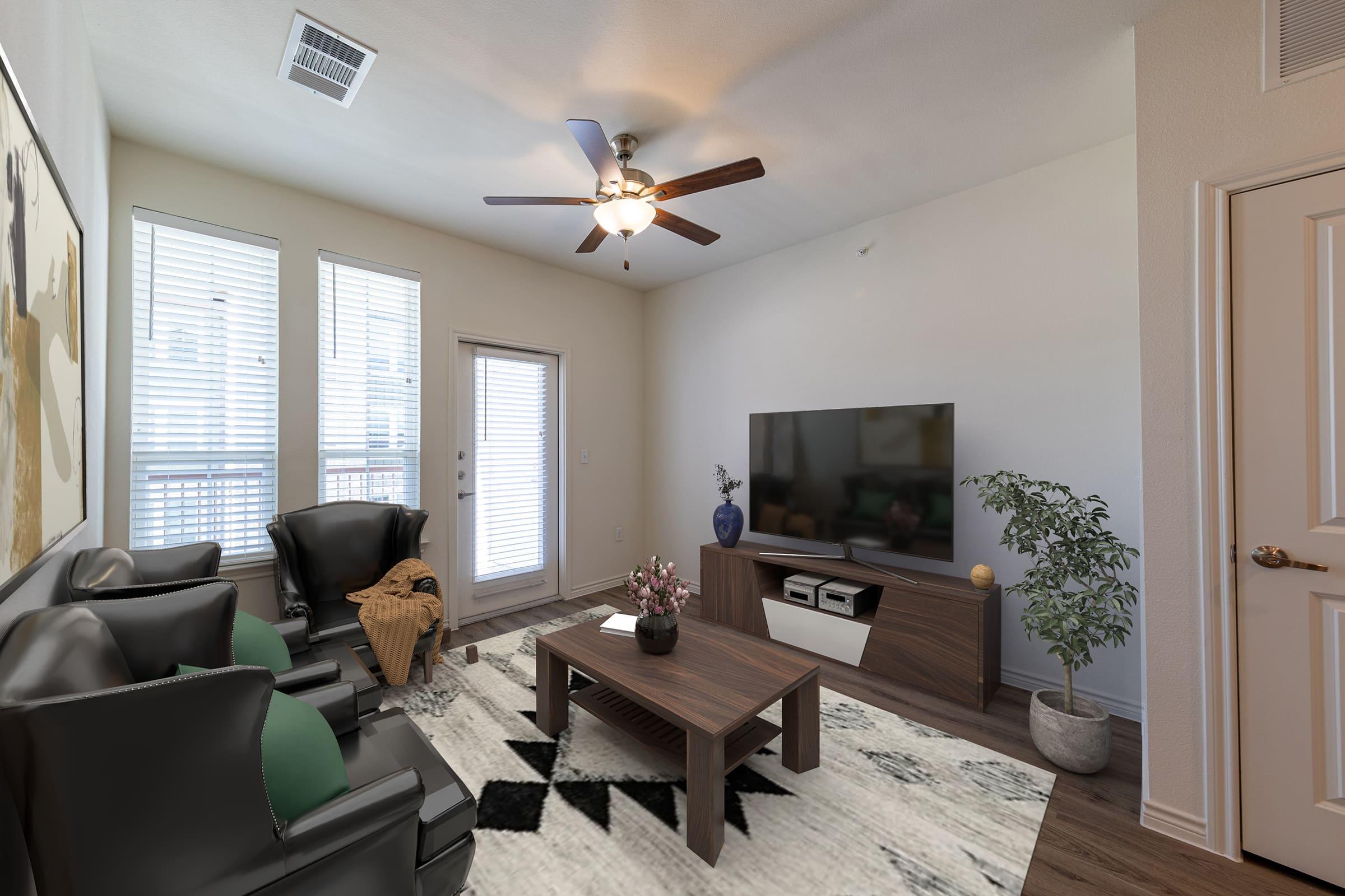 A modern living room featuring two black leather armchairs, a wooden coffee table with a plant and decorative vase, a TV stand with a large television, and a contemporary rug. Natural light streams in through the large windows and glass door leading to a balcony.