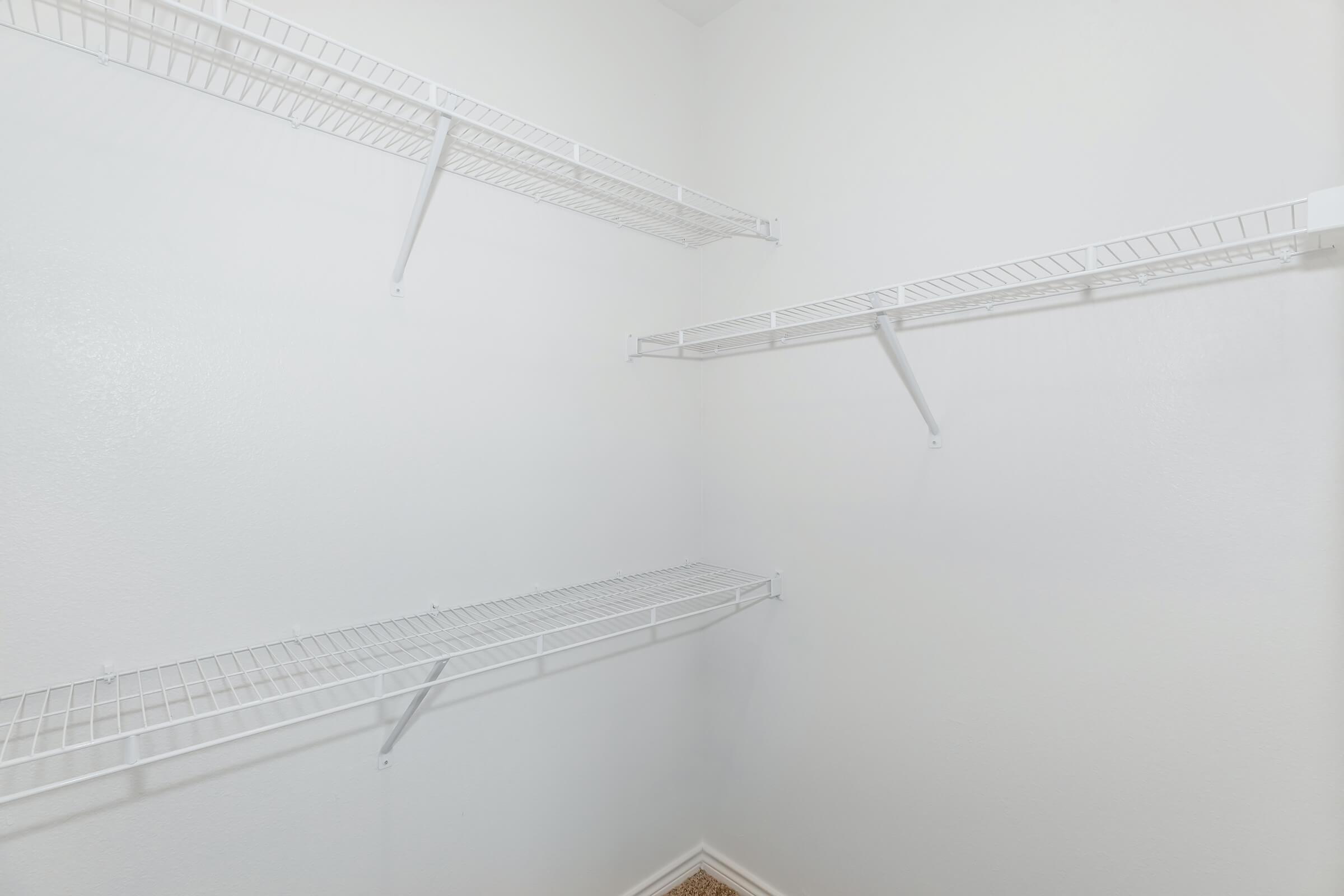 Empty closet with white wire shelving attached to light-colored walls. The space features two shelves on opposite sides, providing a minimalist and organized storage option. The floor is carpeted, adding a touch of comfort to the otherwise bare area.