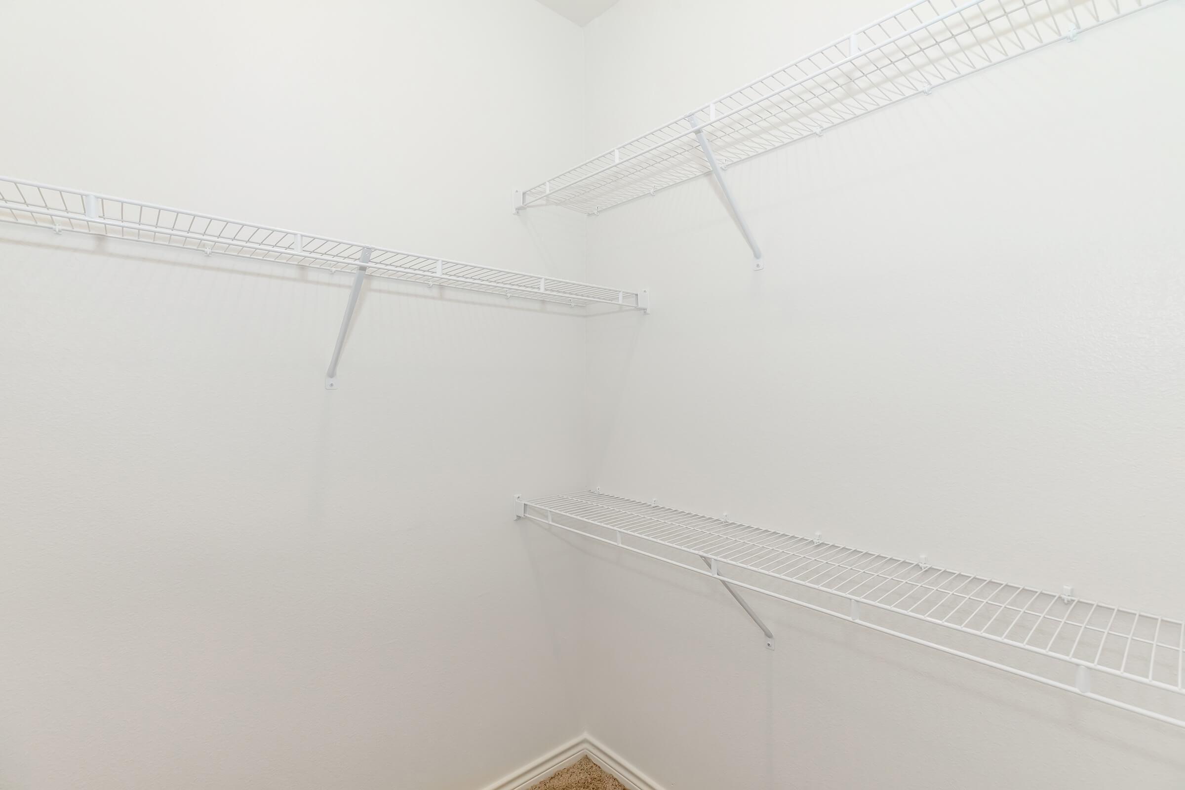 Empty closet with white wire shelving attached to the walls. The walls are painted a light color, and there is no visible clutter or items in the space. The floor appears to be carpeted, and the shelves are arranged at various heights.
