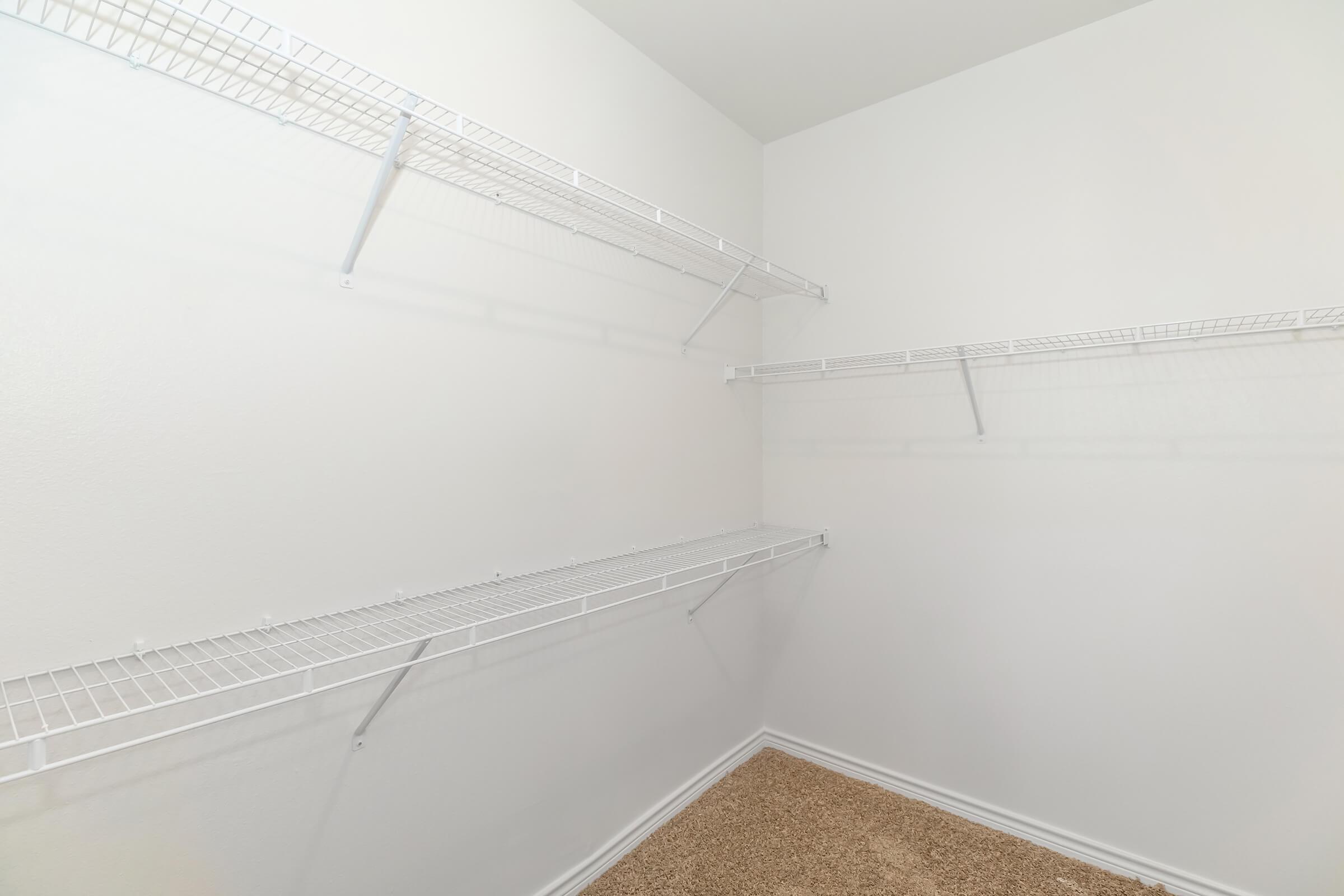 Empty closet with white wire shelving attached to the walls. The walls are painted white, and the floor is covered in beige carpet.