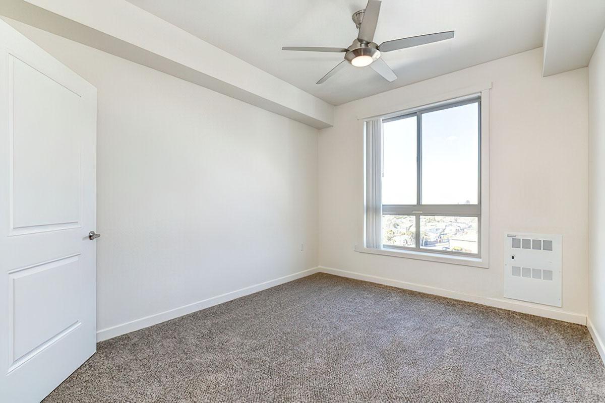 A bright, empty room with light gray walls and a carpeted floor.