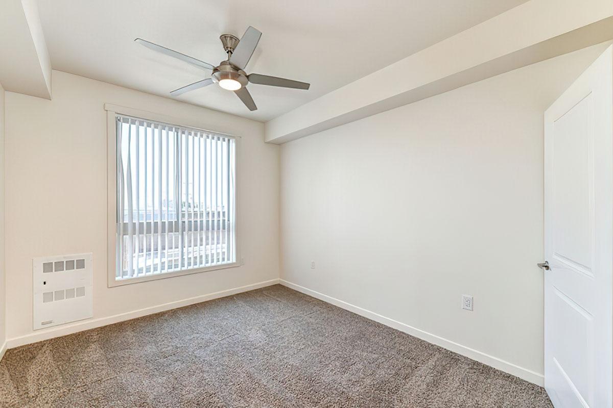 A spacious, unfurnished room with light beige walls and a large window covered by vertical blinds.