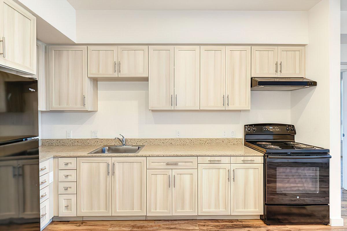 Modern kitchen with light-colored wooden cabinets, a beige countertop, a black oven, and a stainless steel sink.