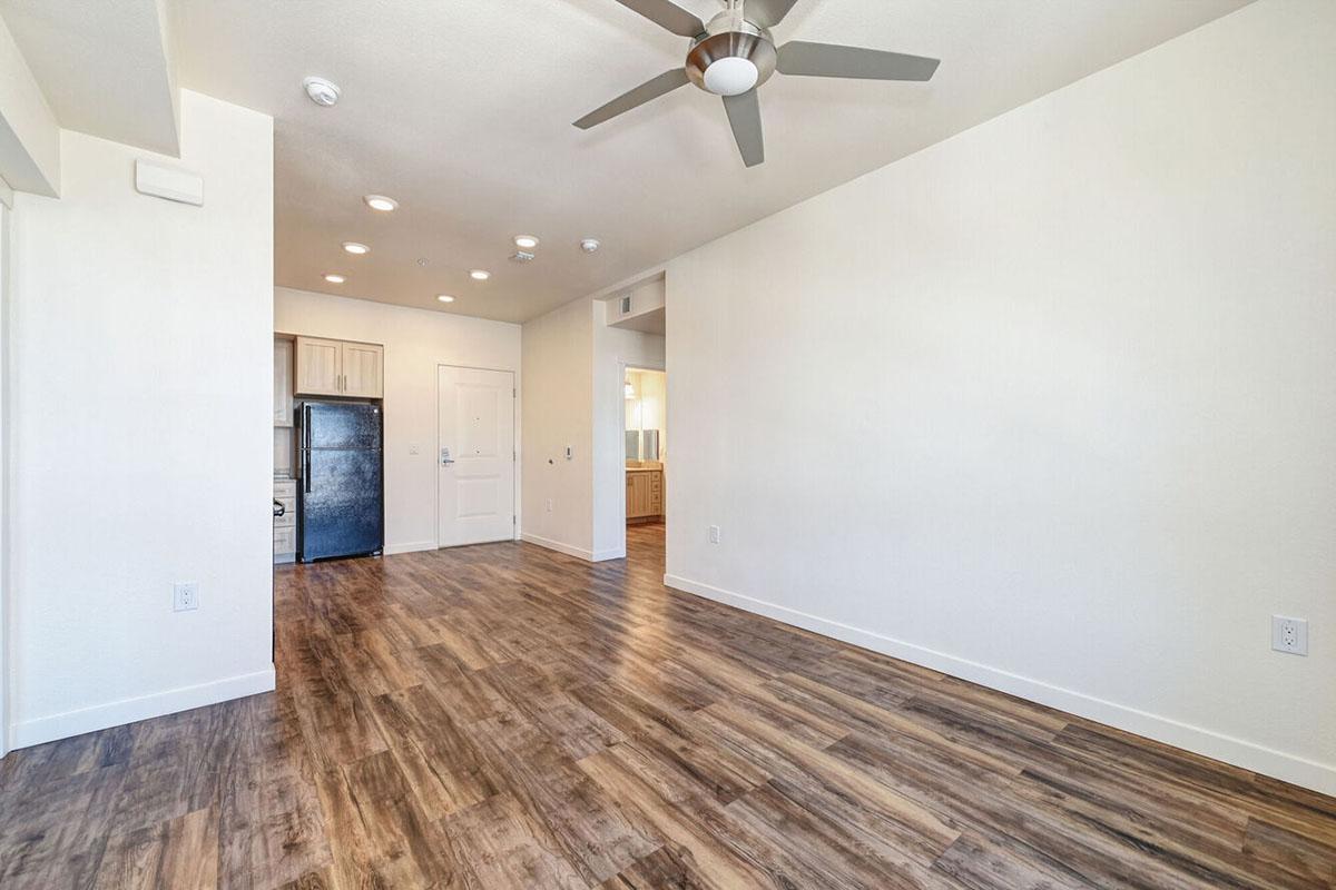A spacious, empty living area featuring light-colored walls and a modern ceiling fan.