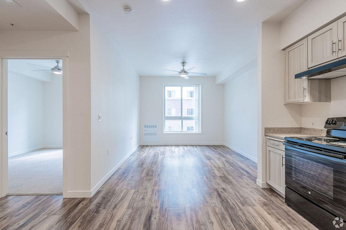 A spacious, modern apartment interior featuring an open layout. The room includes a kitchen area with light-colored cabinetry and an oven.