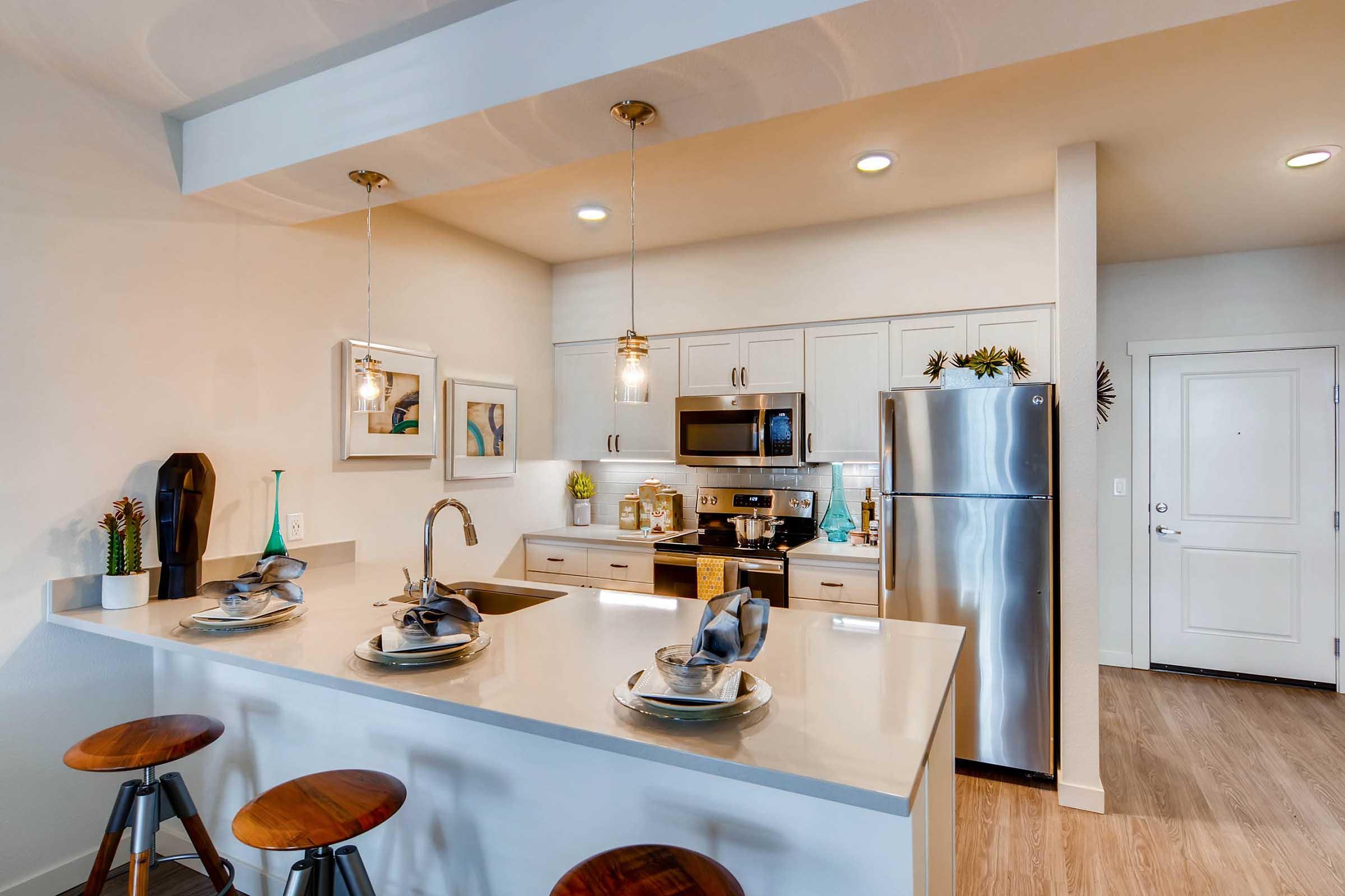 Modern kitchen featuring a sleek design with white cabinets, stainless steel appliances, and a large island with bar stools. Decorative items adorn the counter, and ambient lighting enhances the inviting atmosphere. A door leads to an exterior space.