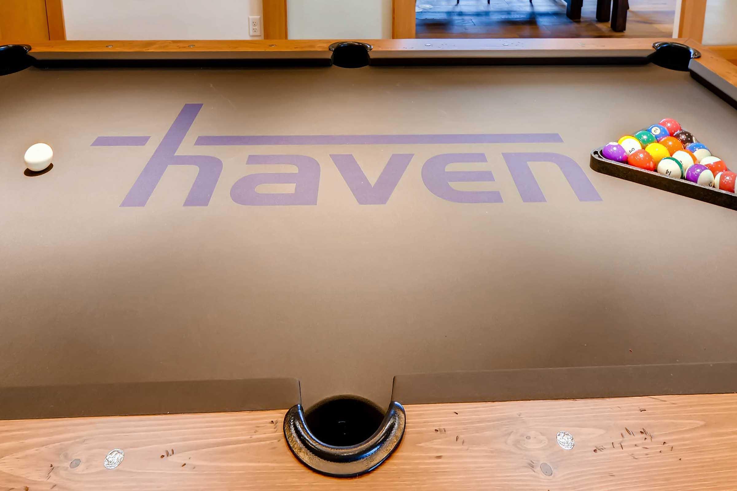 A billiards table with a dark felt surface featuring the word "haven" printed in purple.
