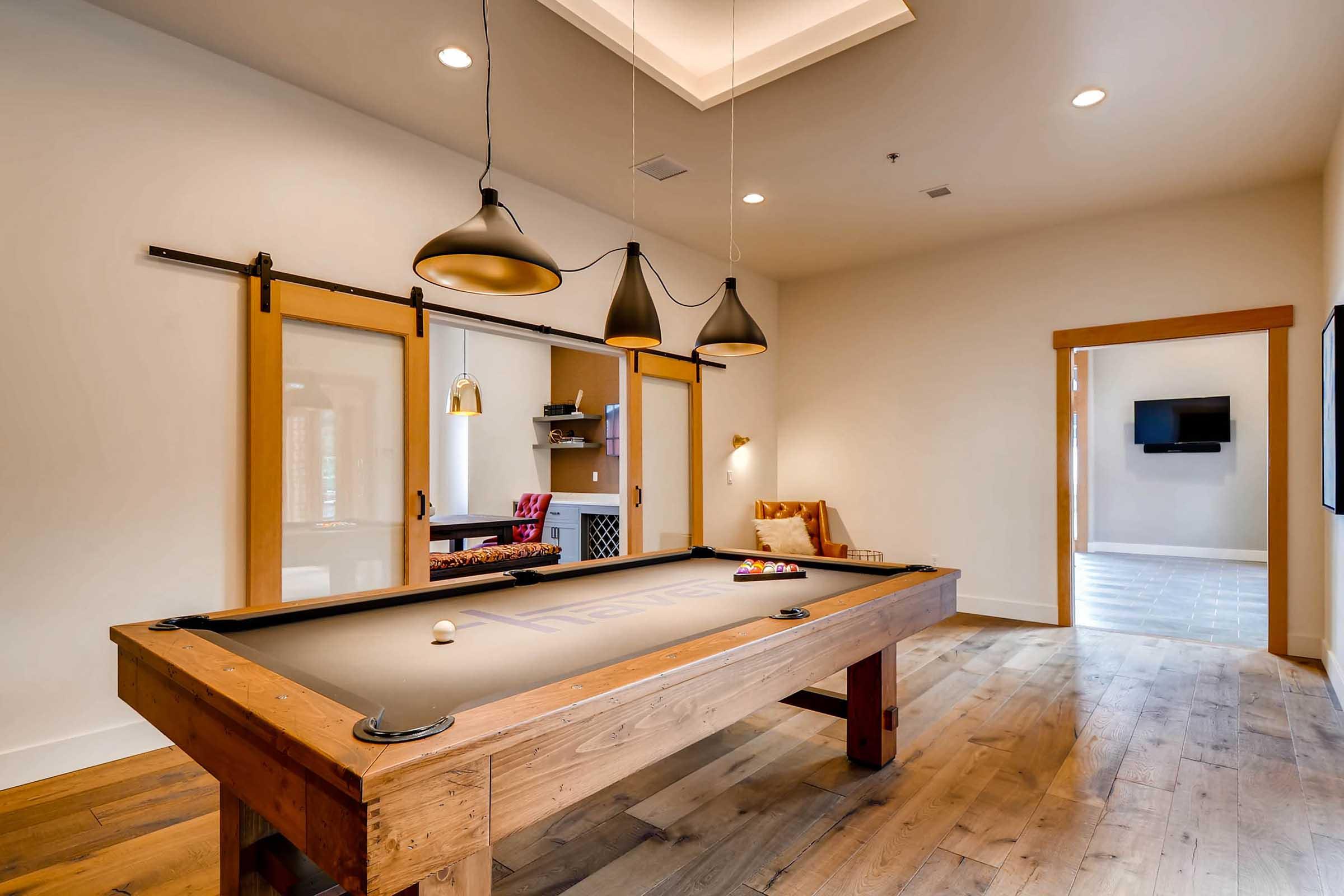A stylish game room featuring a wooden billiards table with a gray felt surface, surrounded by three pendant lamps.
