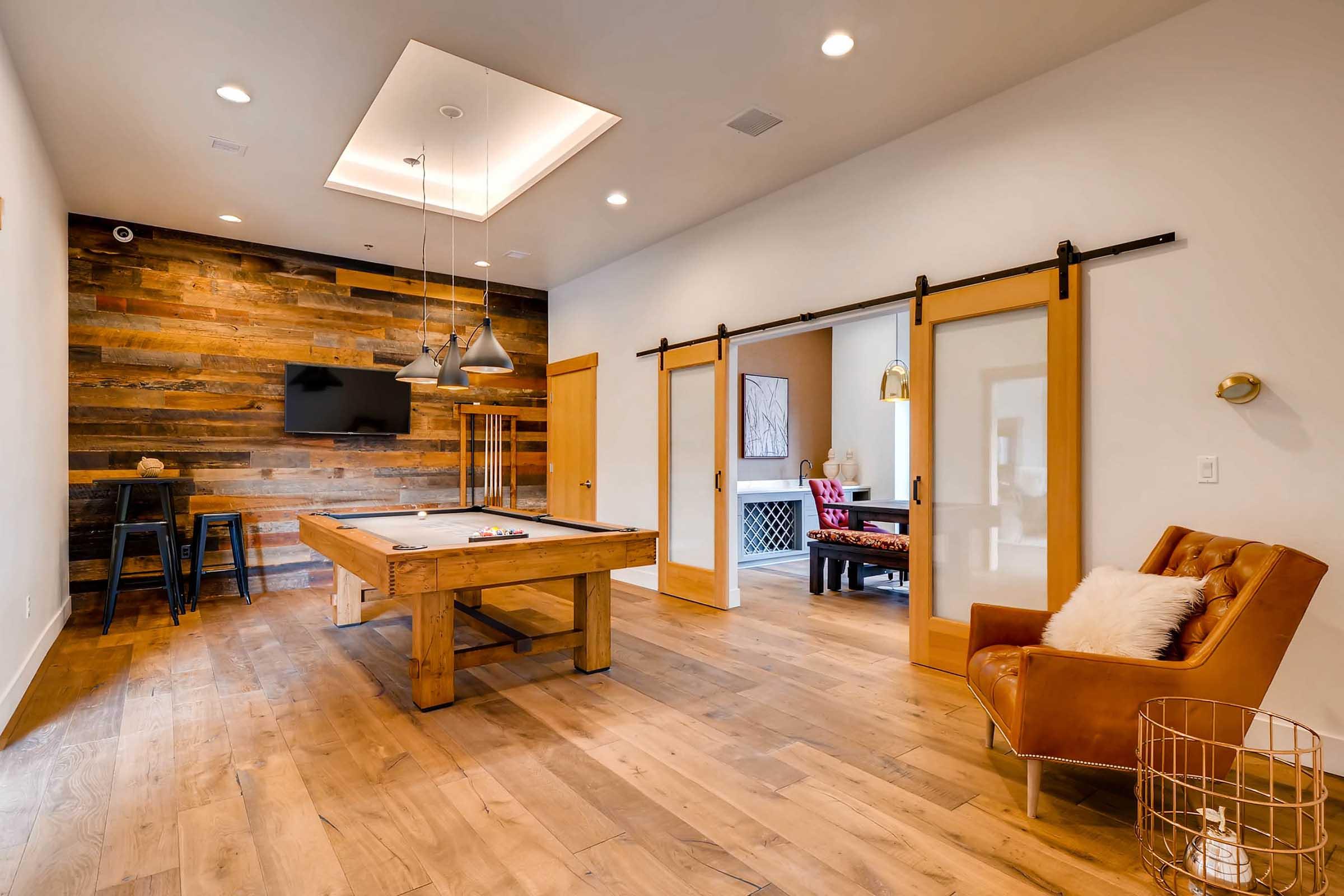 A spacious room featuring a wooden pool table in the center, with large sliding doors on the right leading to another area.