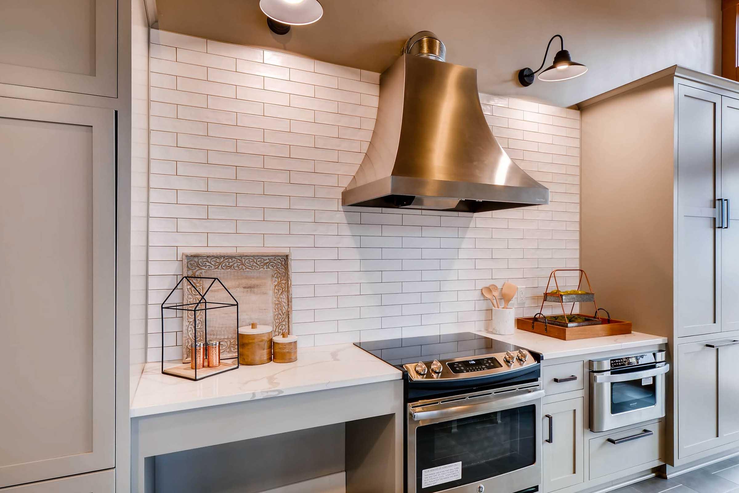 A modern kitchen featuring a stainless steel range hood above a sleek stove, with white subway tile backsplash.